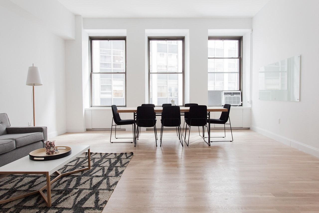 Bright, minimalist living room with hardwood floors, table and chairs, a sofa, and windows.