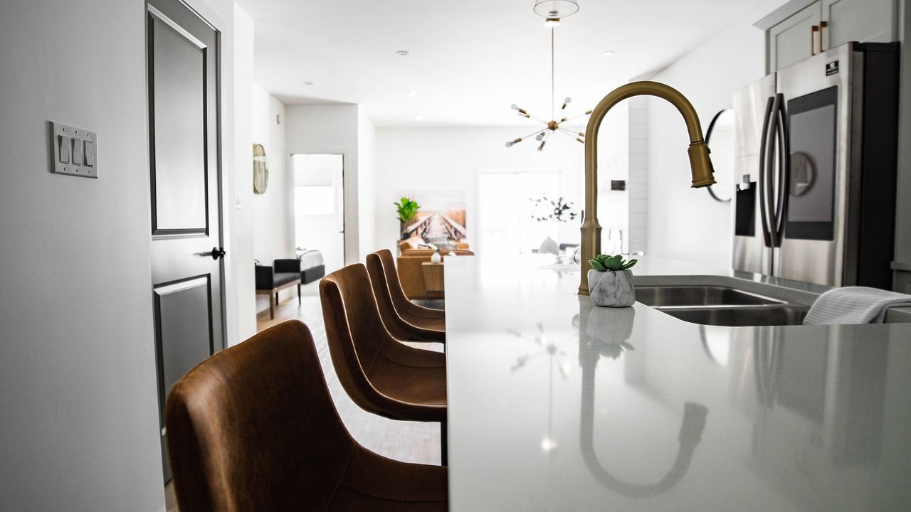 Modern kitchen with a gold faucet, white countertop, and brown bar stools.
