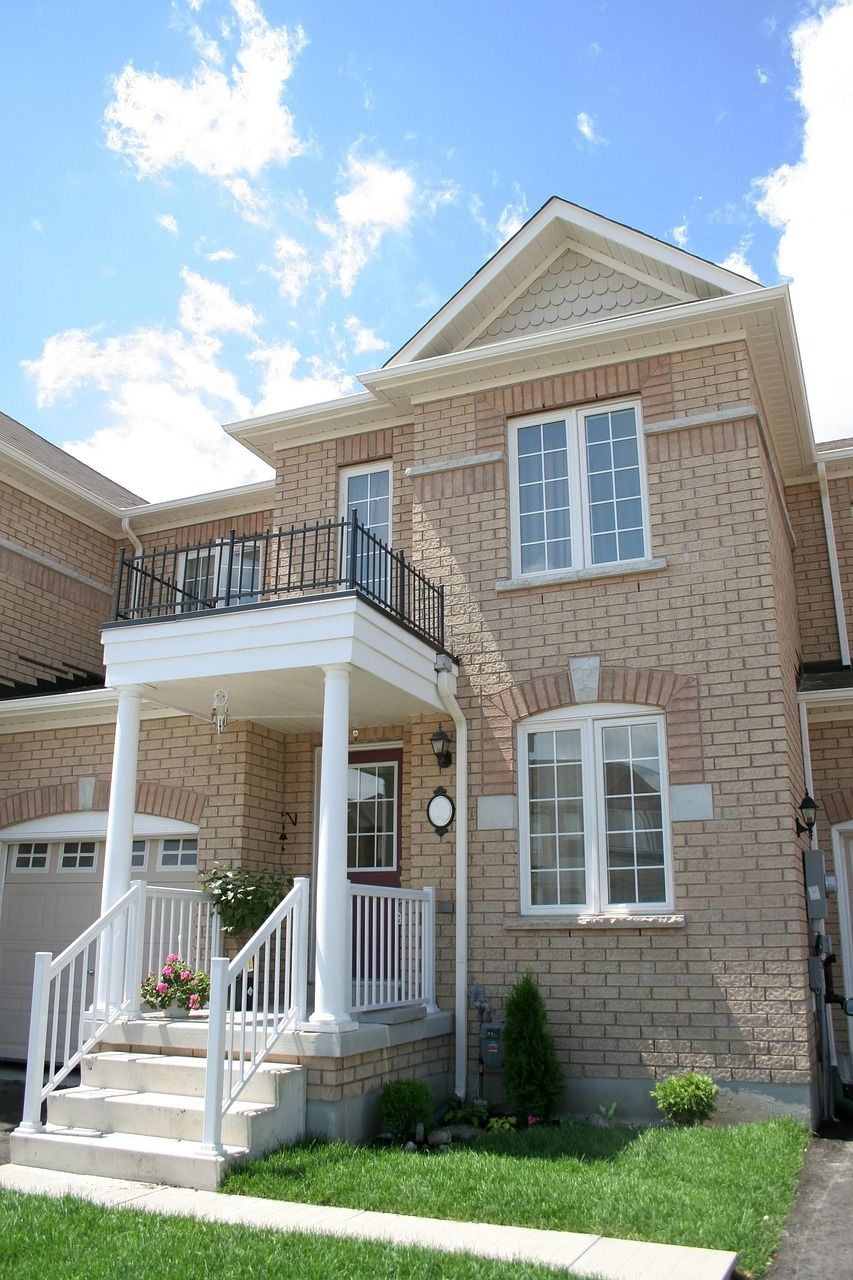 Two-story brick townhouse with a balcony, white trim, and a small front yard with grass.