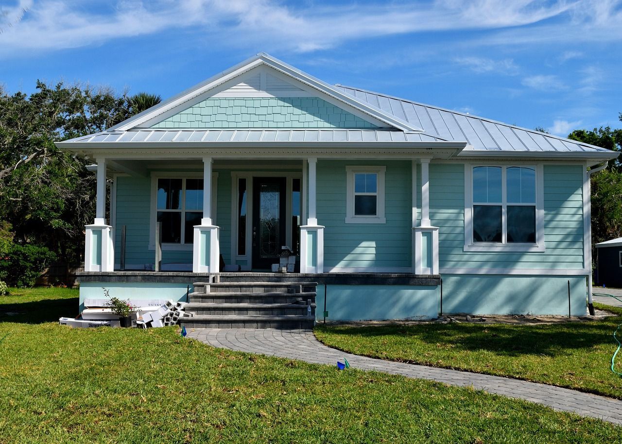Small, light blue house with white trim, porch, and steps. Green grass and blue sky.