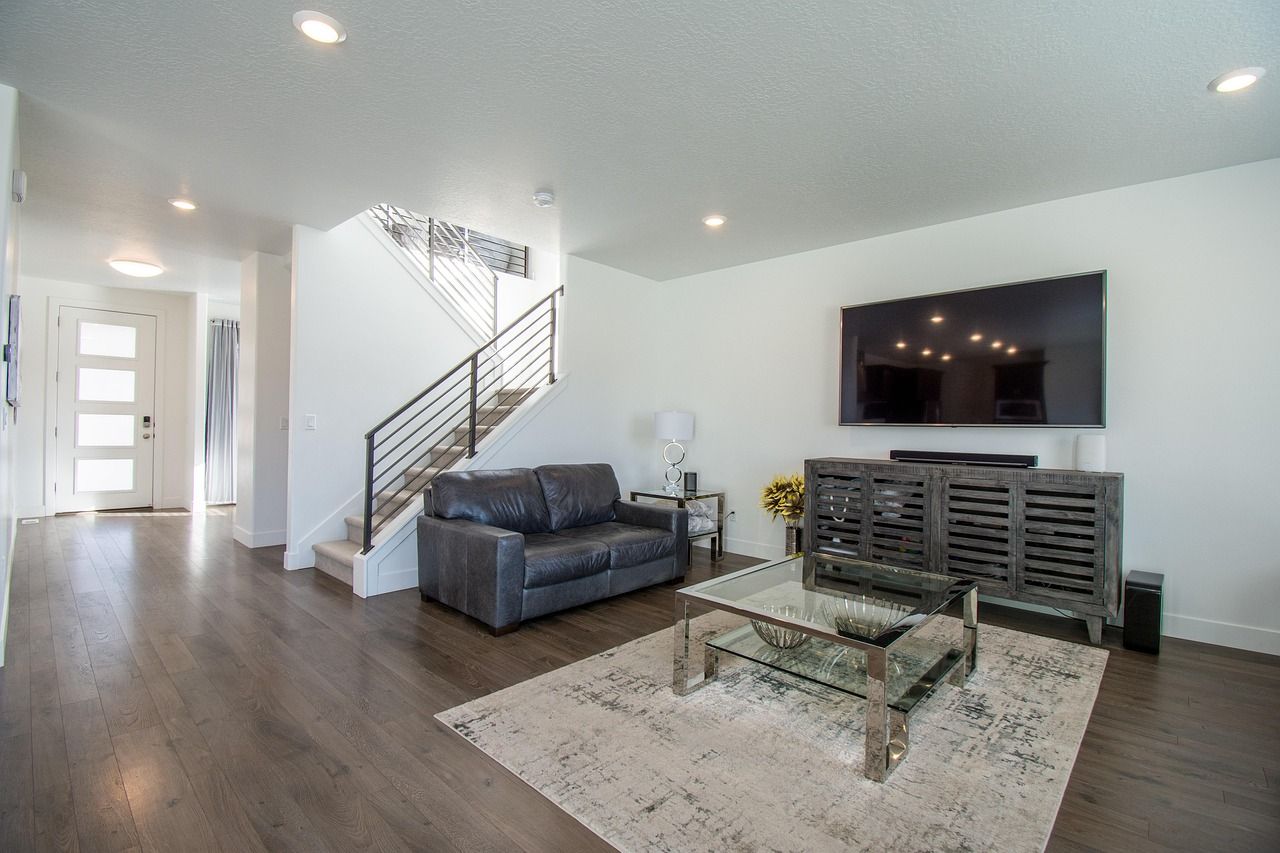 Modern living room with gray sofa, large TV, stairs, and a coffee table on a rug.