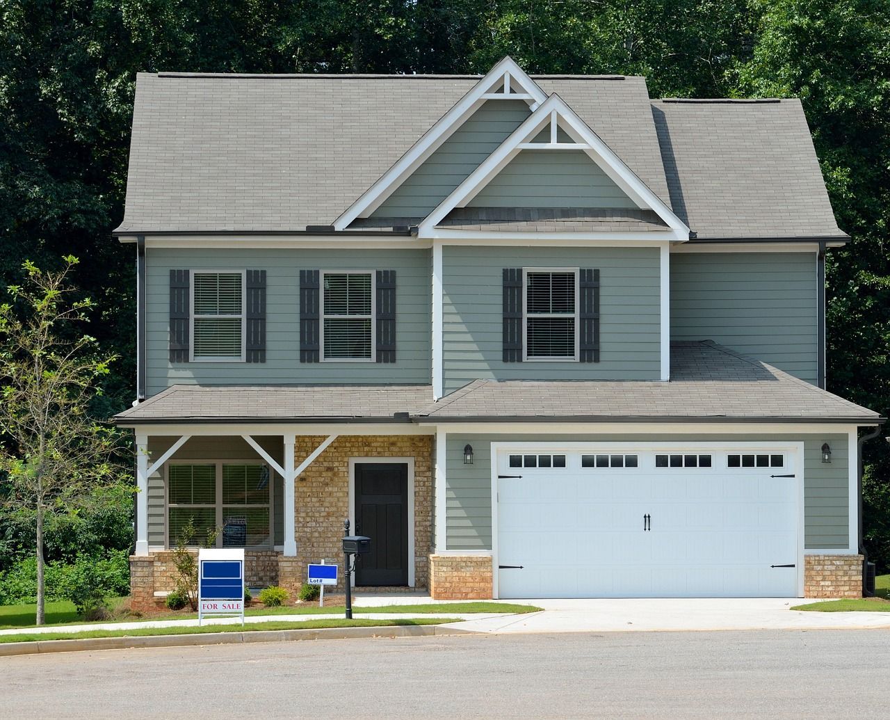 Two-story house, light green siding, gray roof, white garage door, and a for sale sign.