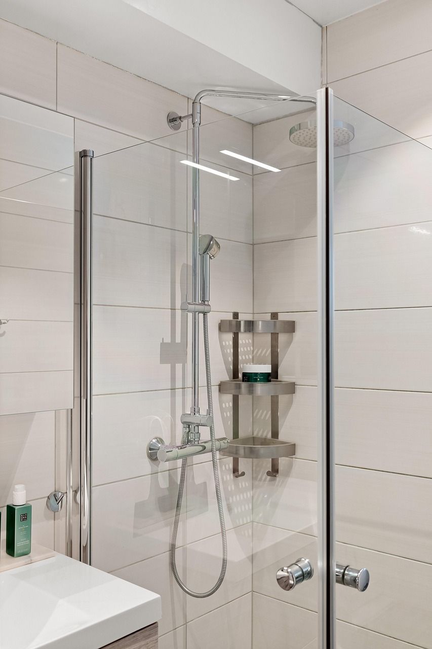 Shower with glass doors, stainless steel fixtures, and white tiled walls.