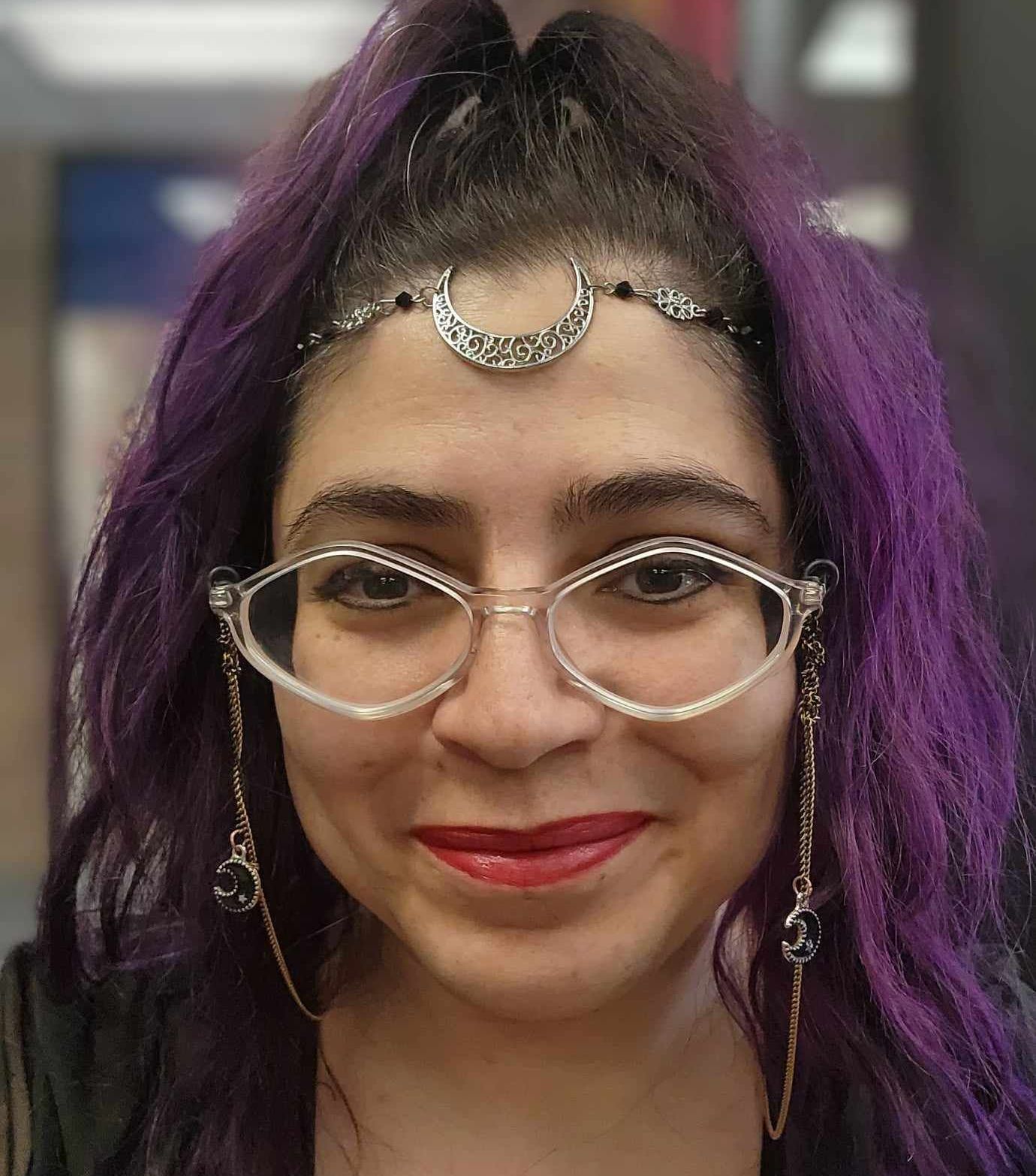 A woman with purple hair and glasses is smiling for the camera.