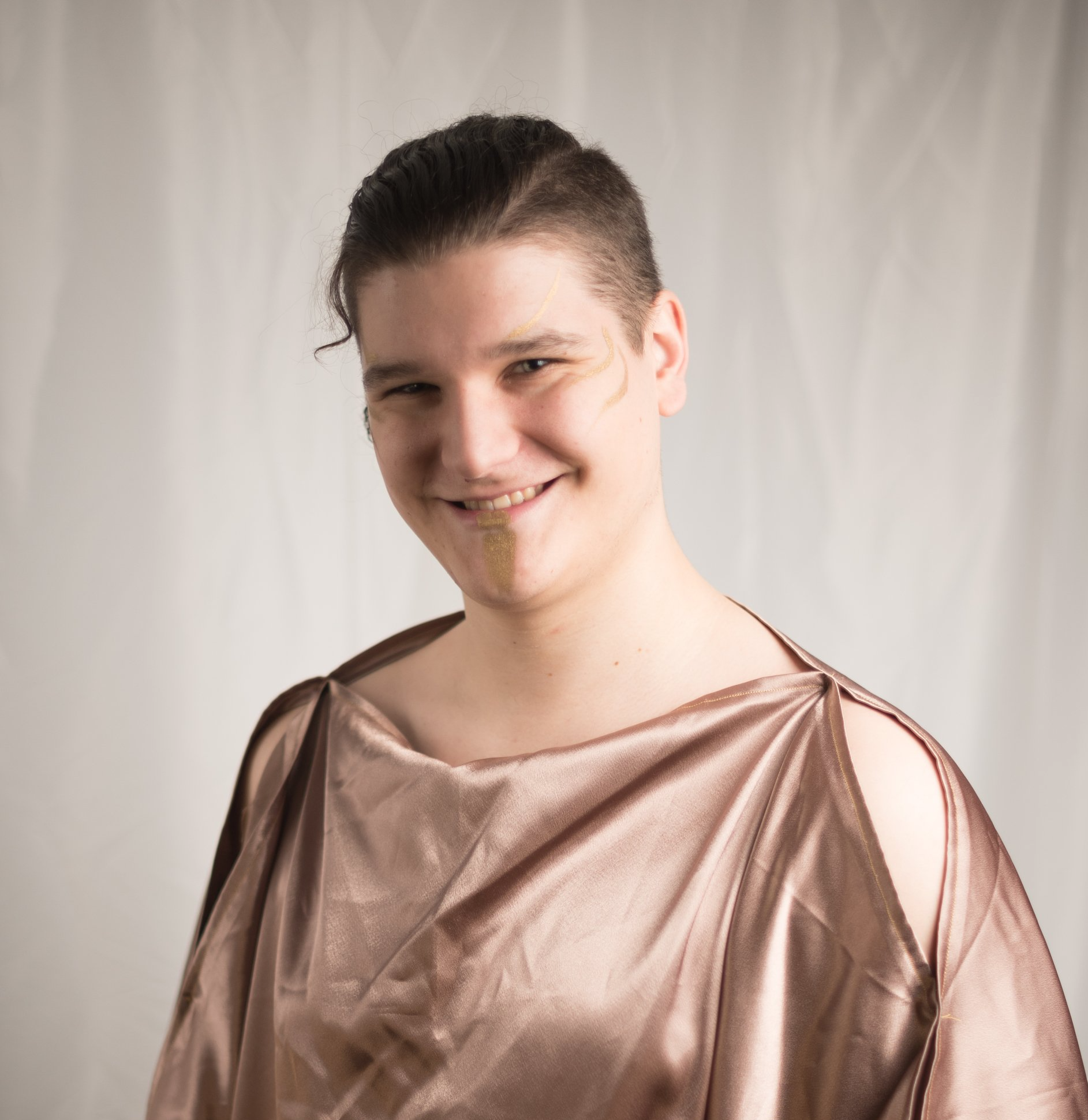 A young man wearing a brown satin toga smiling, representing Apollo.