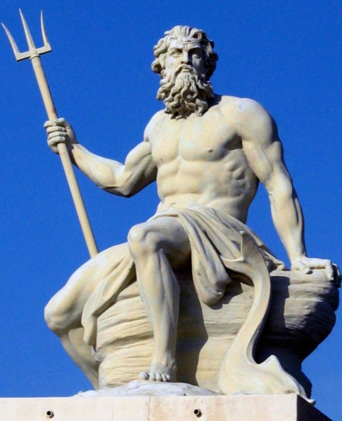 A statue of a man holding a trident against a blue sky,  representing Poseidon. 