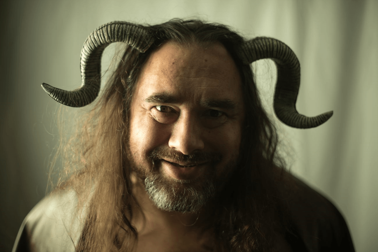 A man with long hair and a beard is wearing horns on his head, representing Pan.