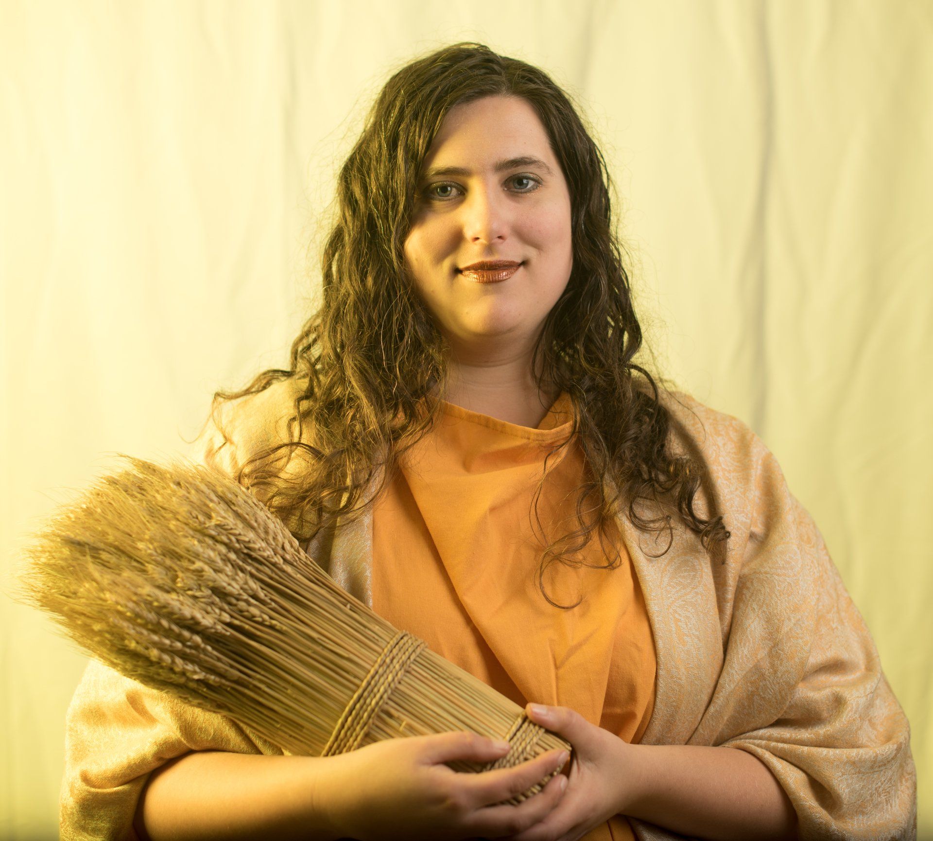 A woman is holding a bunch of wheat in her hands,  representing Demeter.