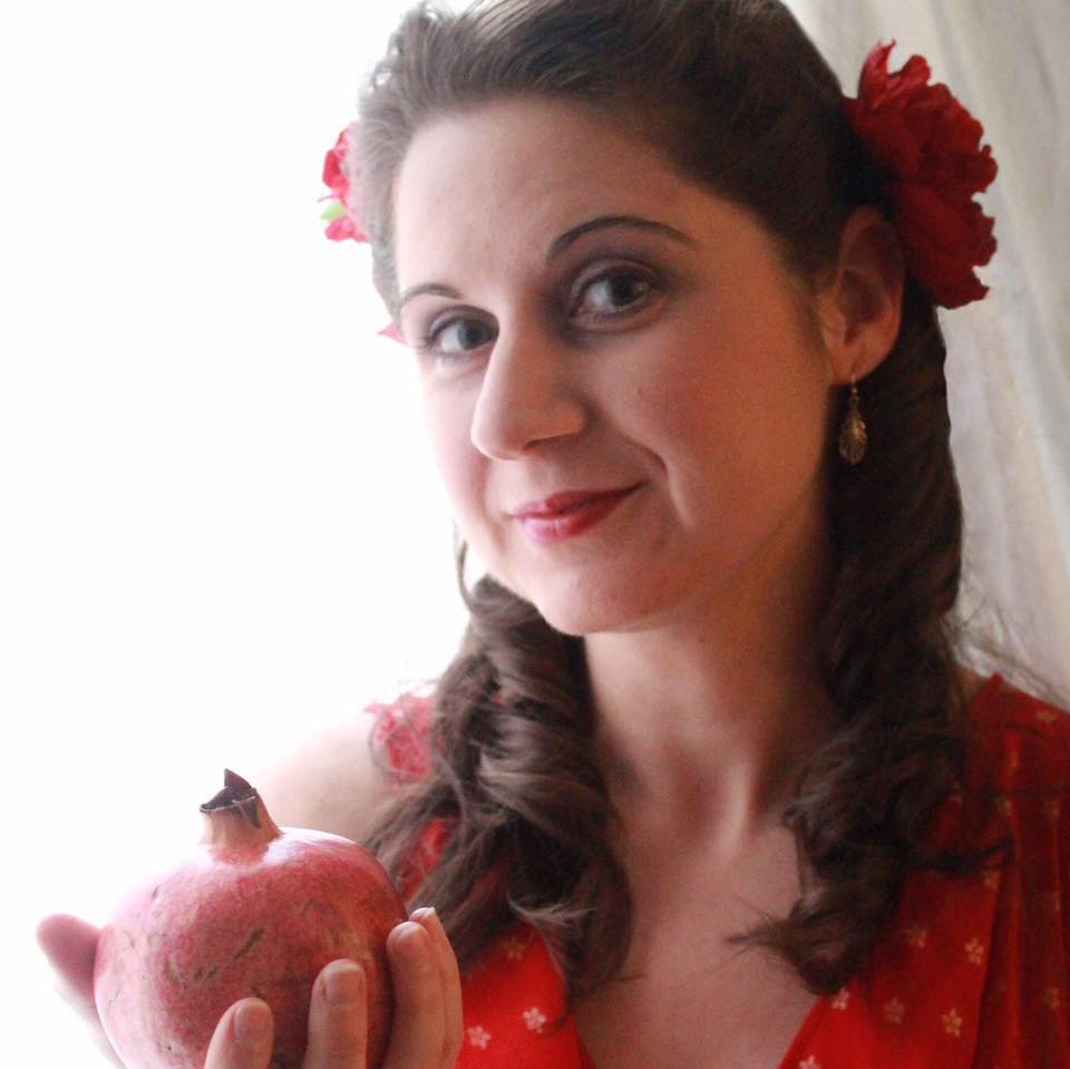 A woman with a flower in her hair is holding a pomegranate, representing Persephone.