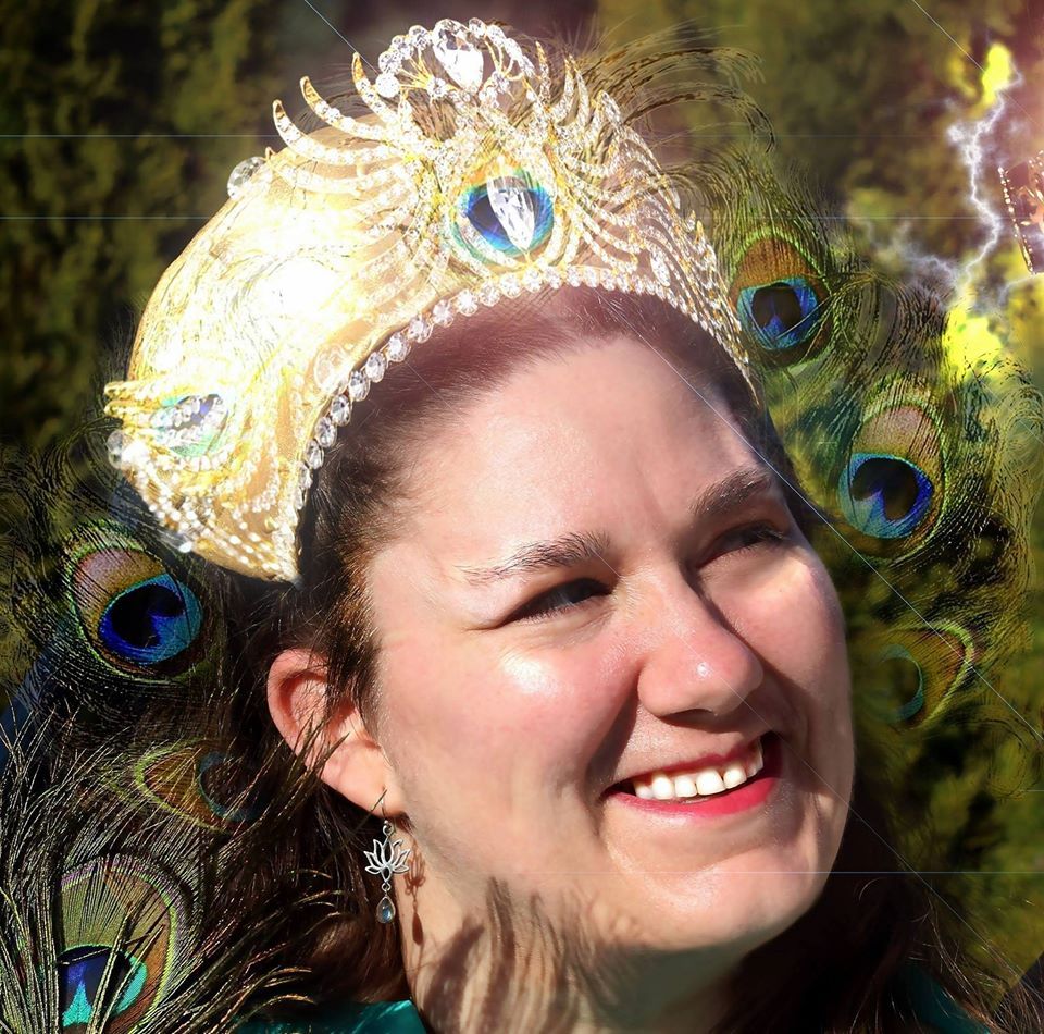 A woman wearing a peacock feather crown is smiling, representing Hera.