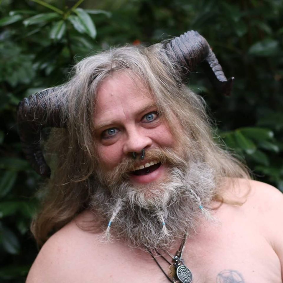 A man with a beard and horns has a tattoo on his chest,  representing Pan.