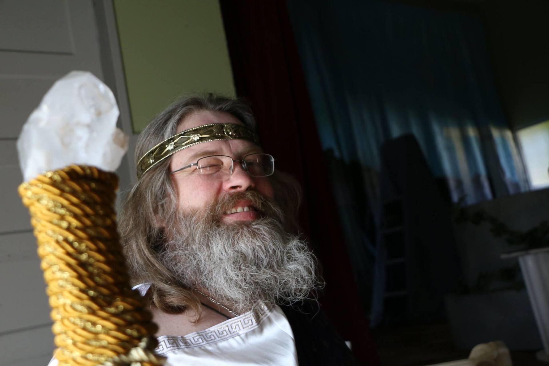 A man with a beard and glasses is holding a crystal in his hand, representing Zeus.