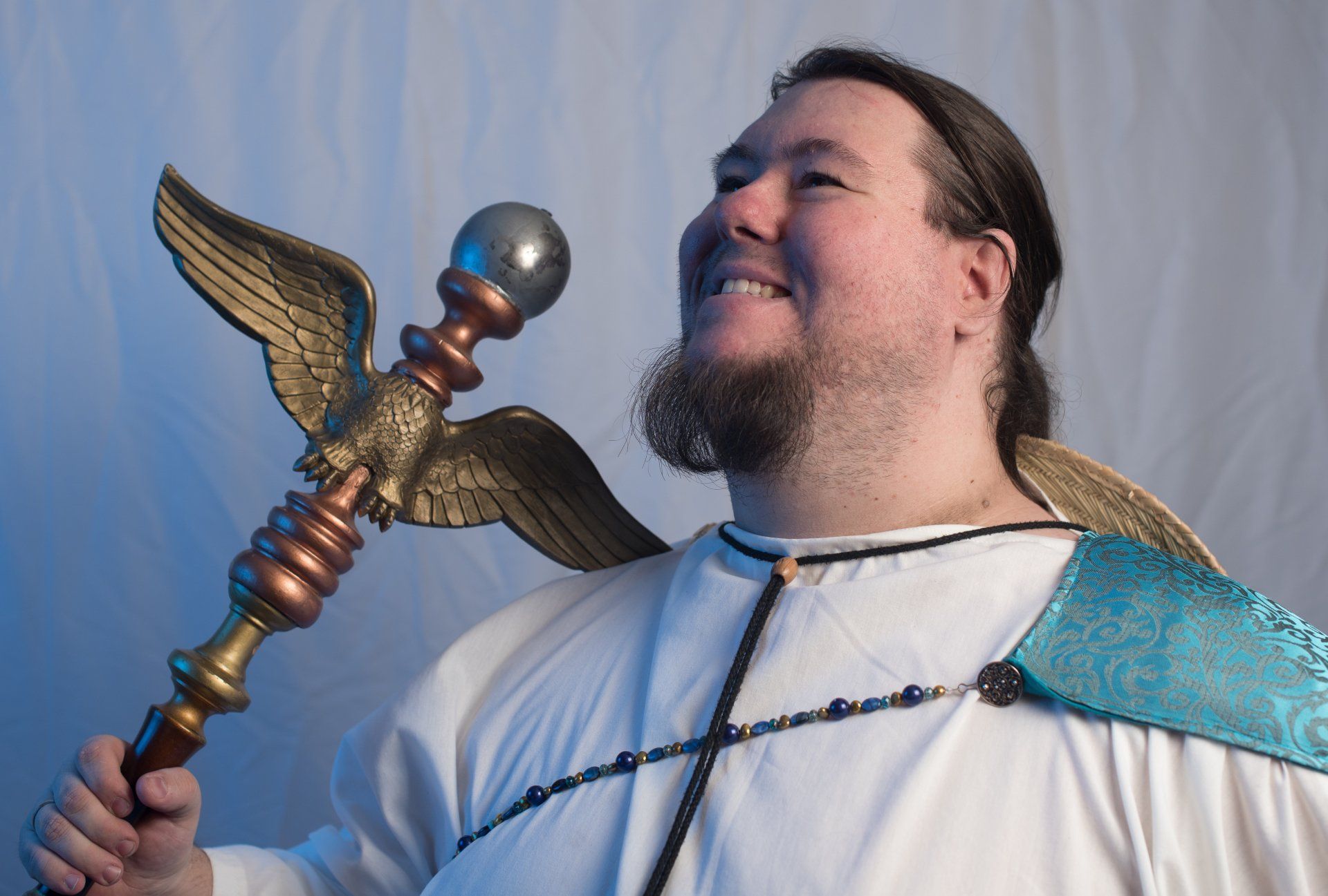 A man with a beard is holding a staff with wings, representing Hermes.