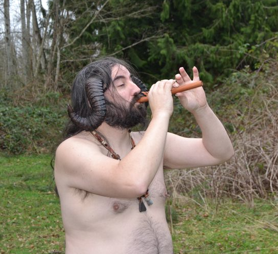 A shirtless man with horns on his head is playing a flute,  representing Pan.