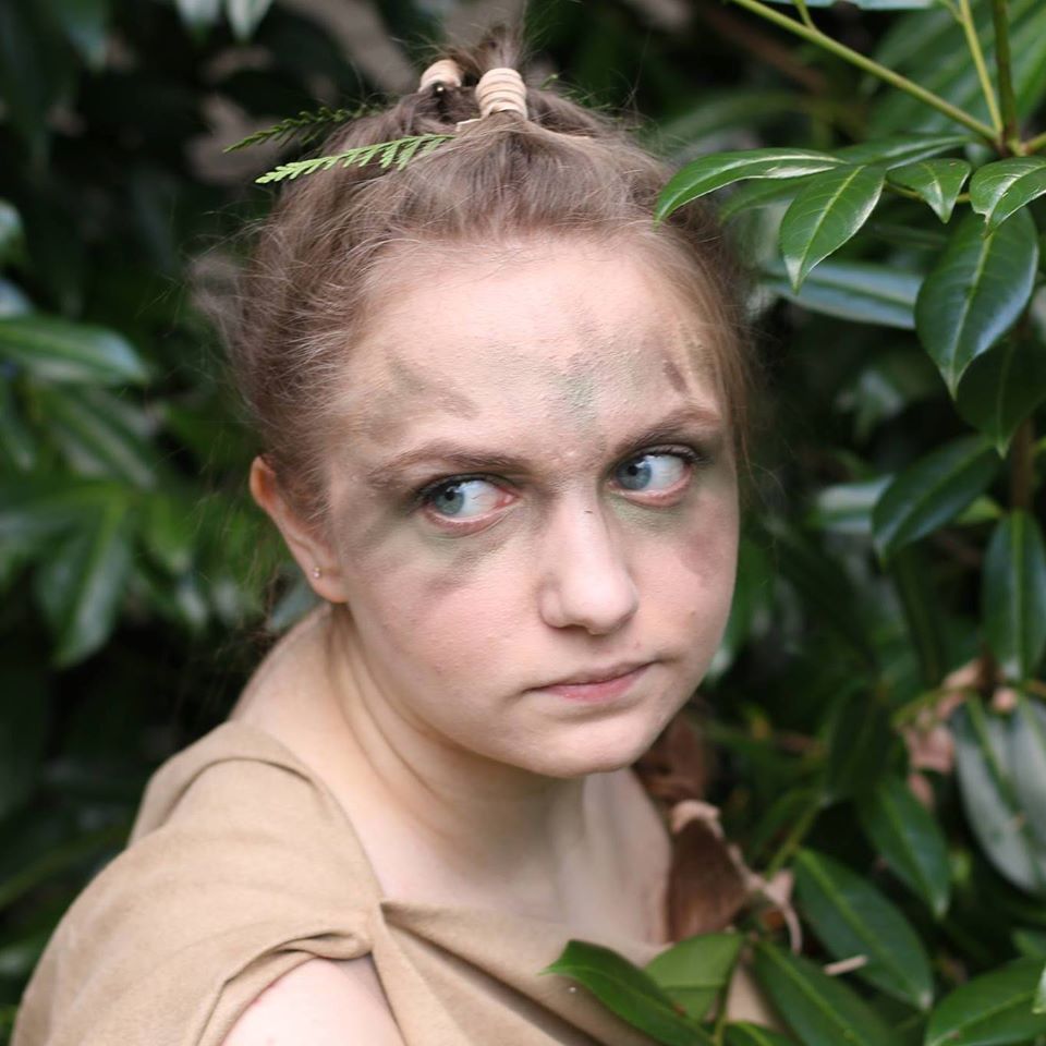 A close up of a woman 's face with leaves in the background,  representing Artemis.
