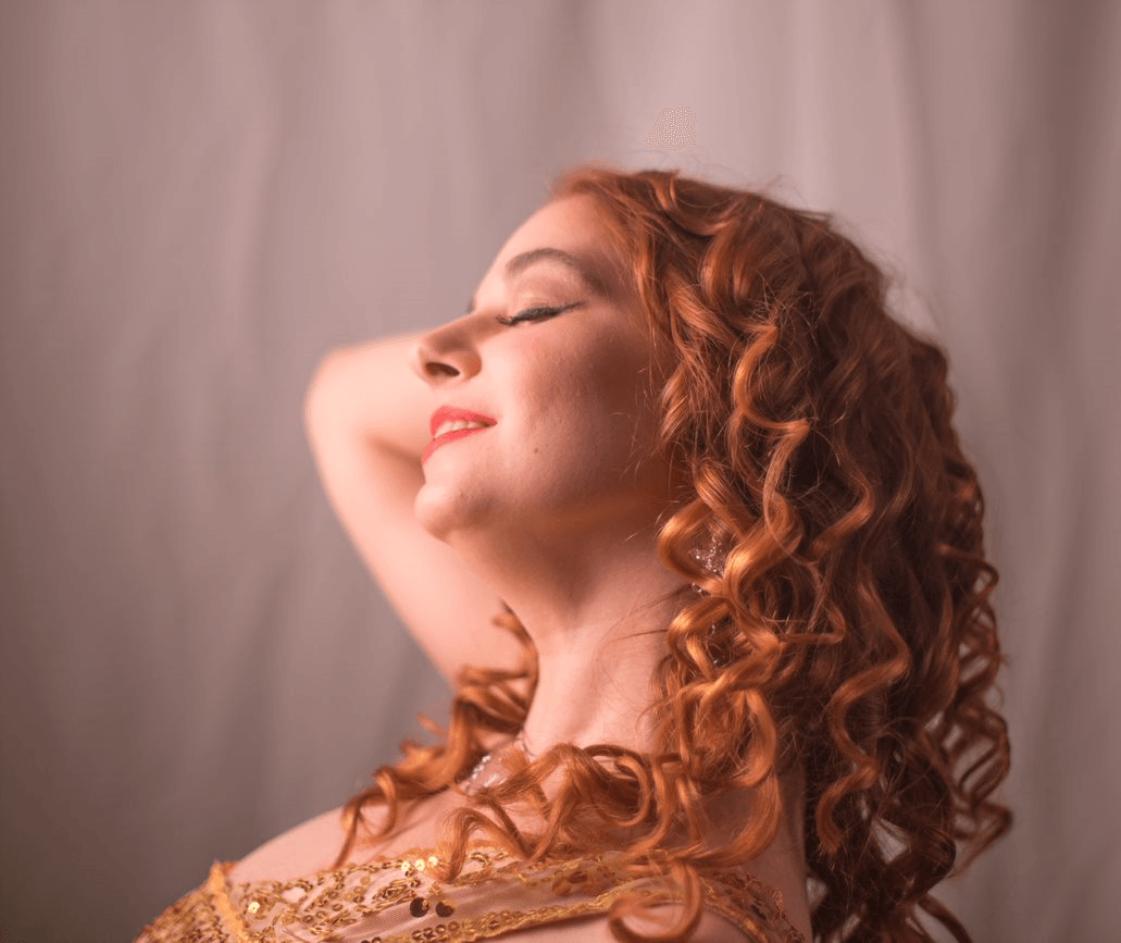 A woman with red curly hair is smiling with her eyes closed, representing Aphrodite.