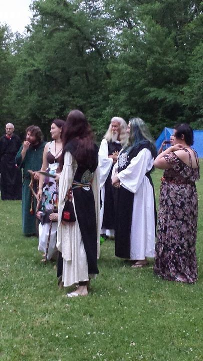 A group of people in medieval costumes are standing in a grassy field, members of the Aquarian Tabernacle Church.