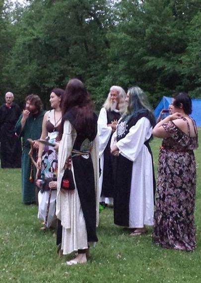 A group of people in medieval costumes are standing in a grassy field, members of the Aquarian Tabernacle Church.