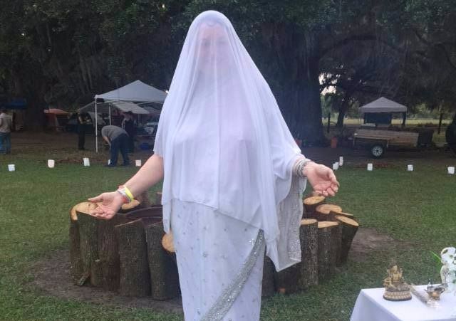 A woman in a white dress is standing in a field and ritual circle.