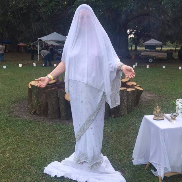 A woman in a white dress is standing in a field and ritual circle.