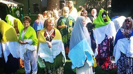 A group of people are standing in the grass covered in shawls.