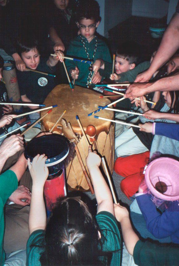 A group of children are playing with sticks around a drum