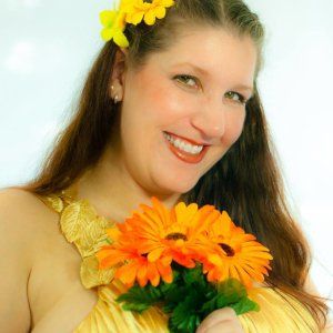 A woman in a gold dress is holding a bouquet of orange flowers.
