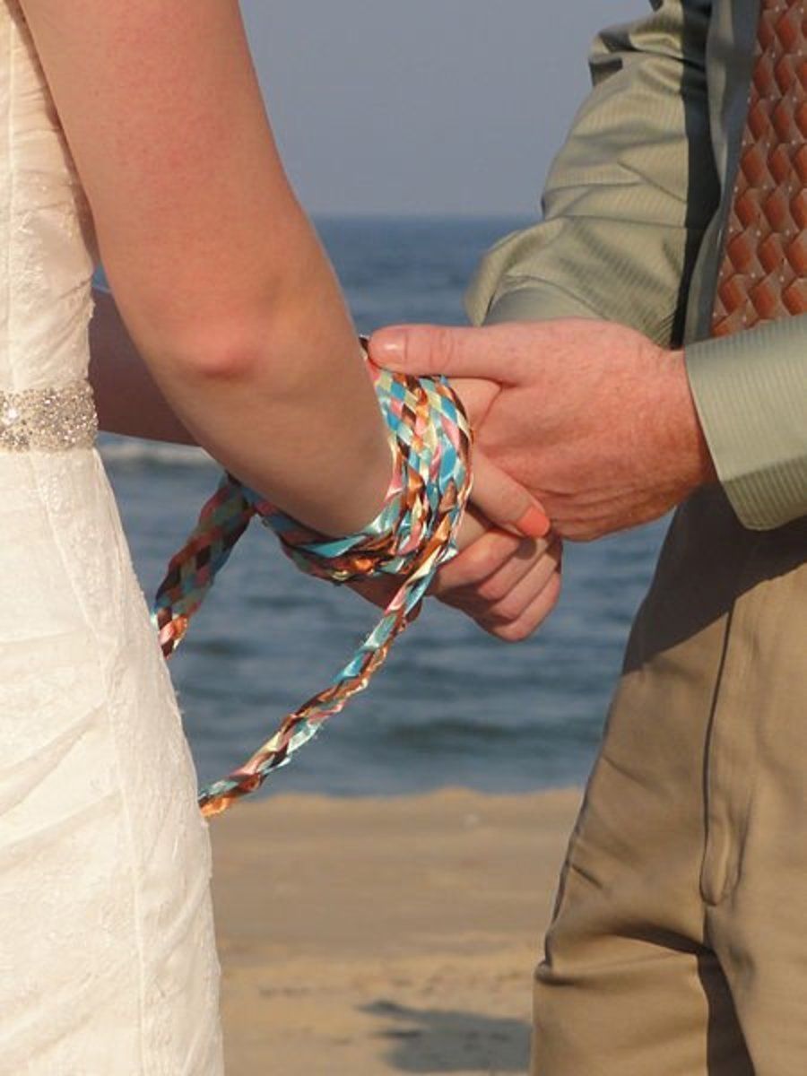 A bride and groom holding hands on the beach in handfasting.