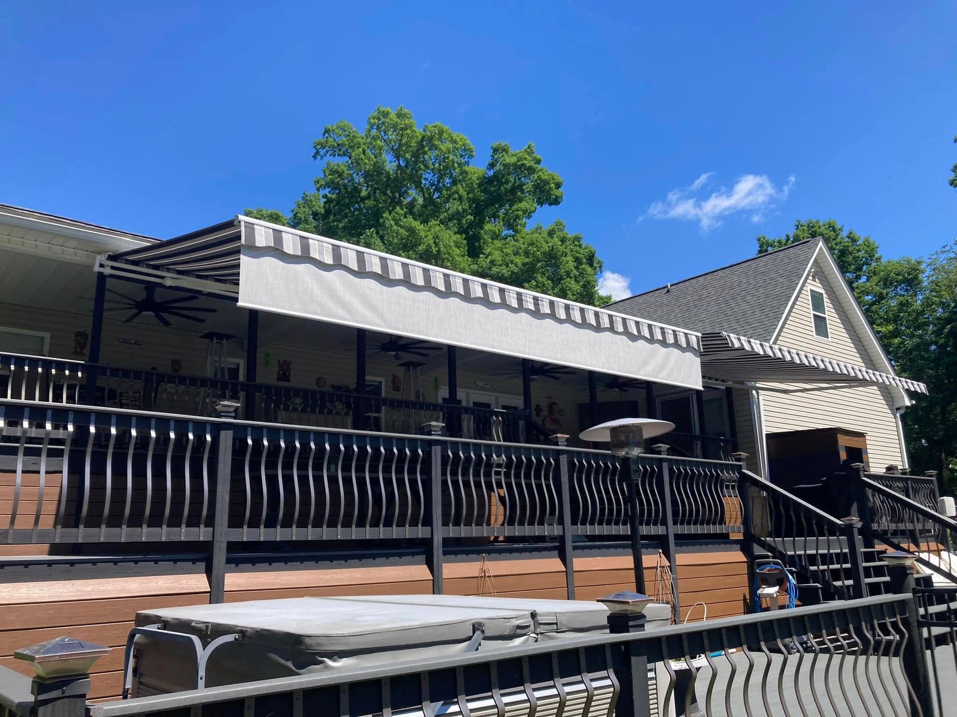Outdoor restaurant patio with awnings and a black railing against a bright blue sky.