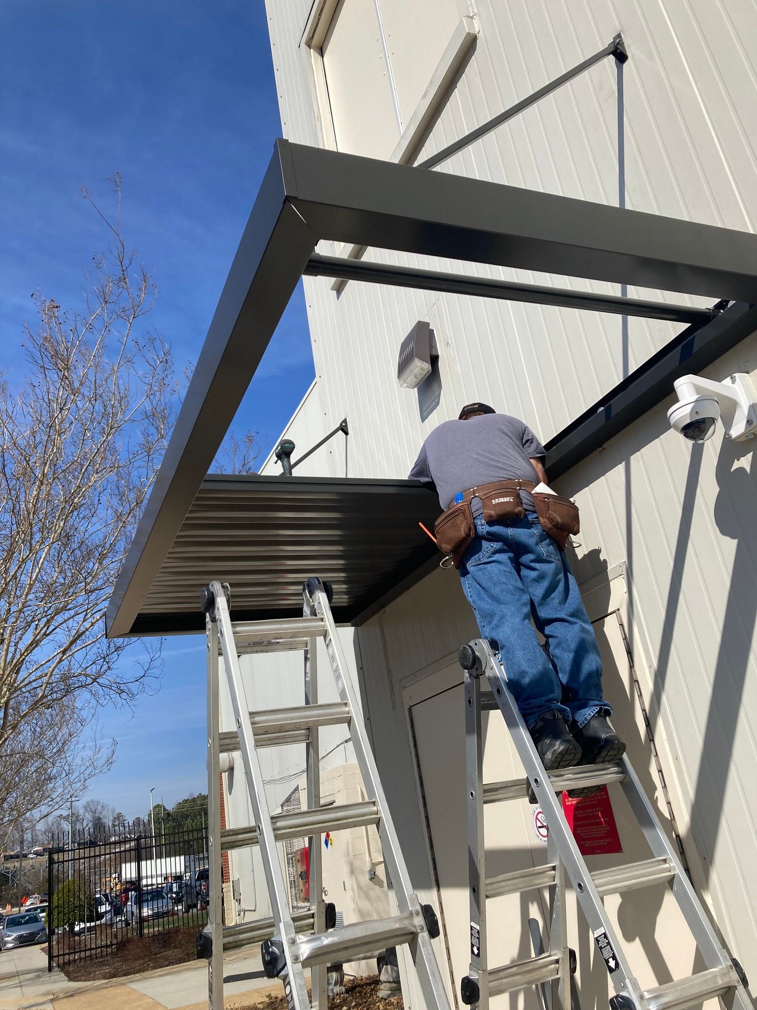 Person on ladder installing awning on white building. Bright sunny day.