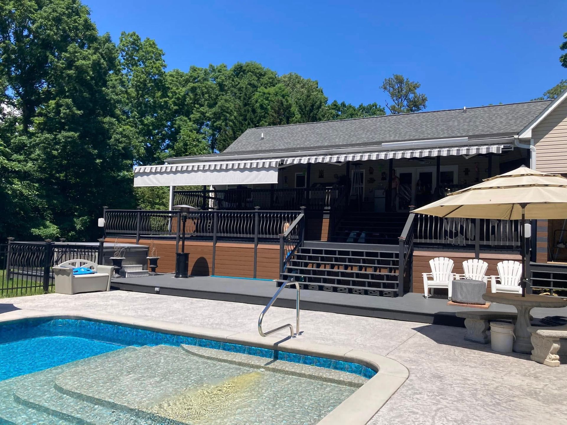 Poolside deck with awning, steps, and pool on a sunny day.