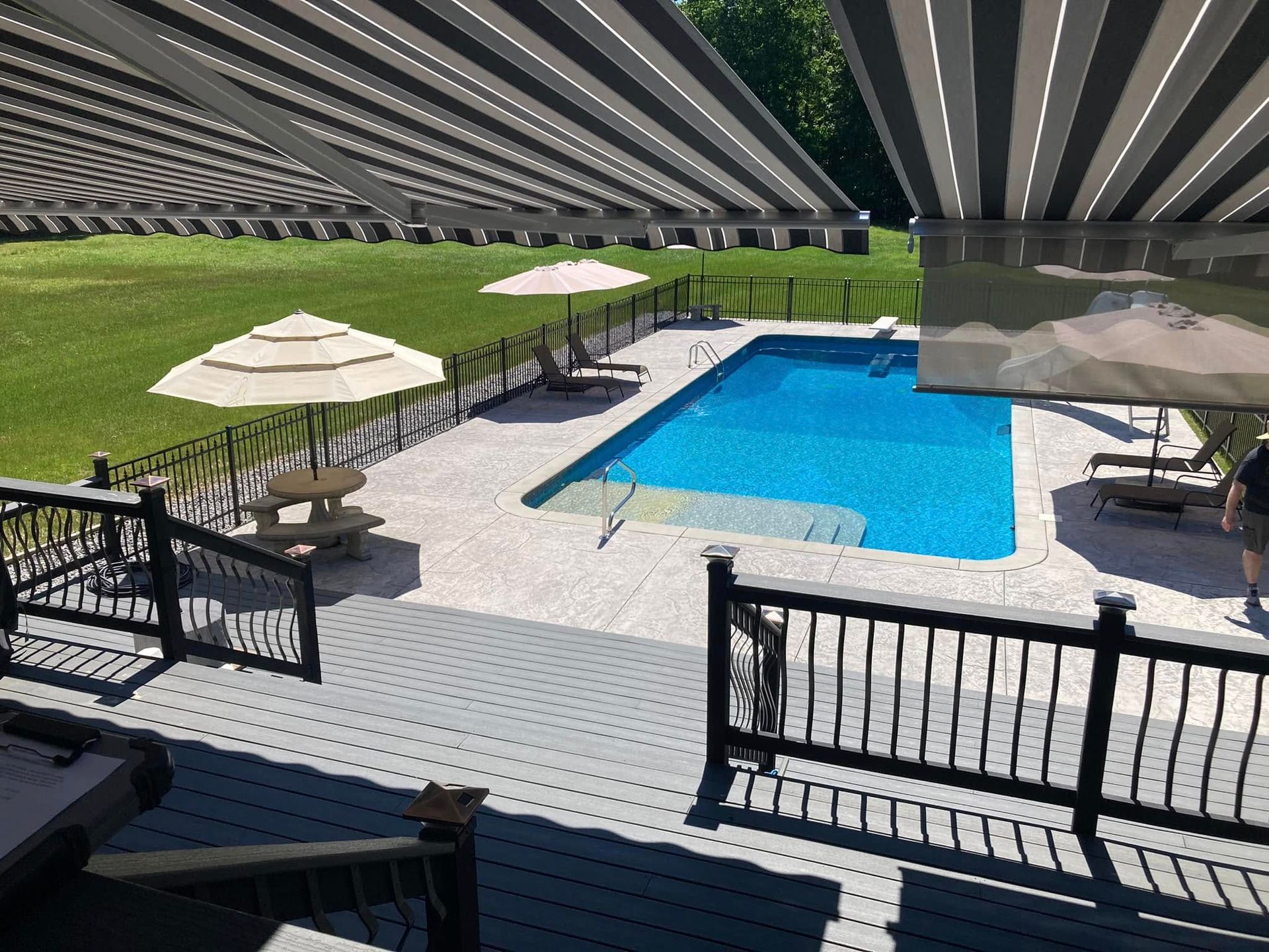 Pool area with deck, umbrellas, and striped awning.