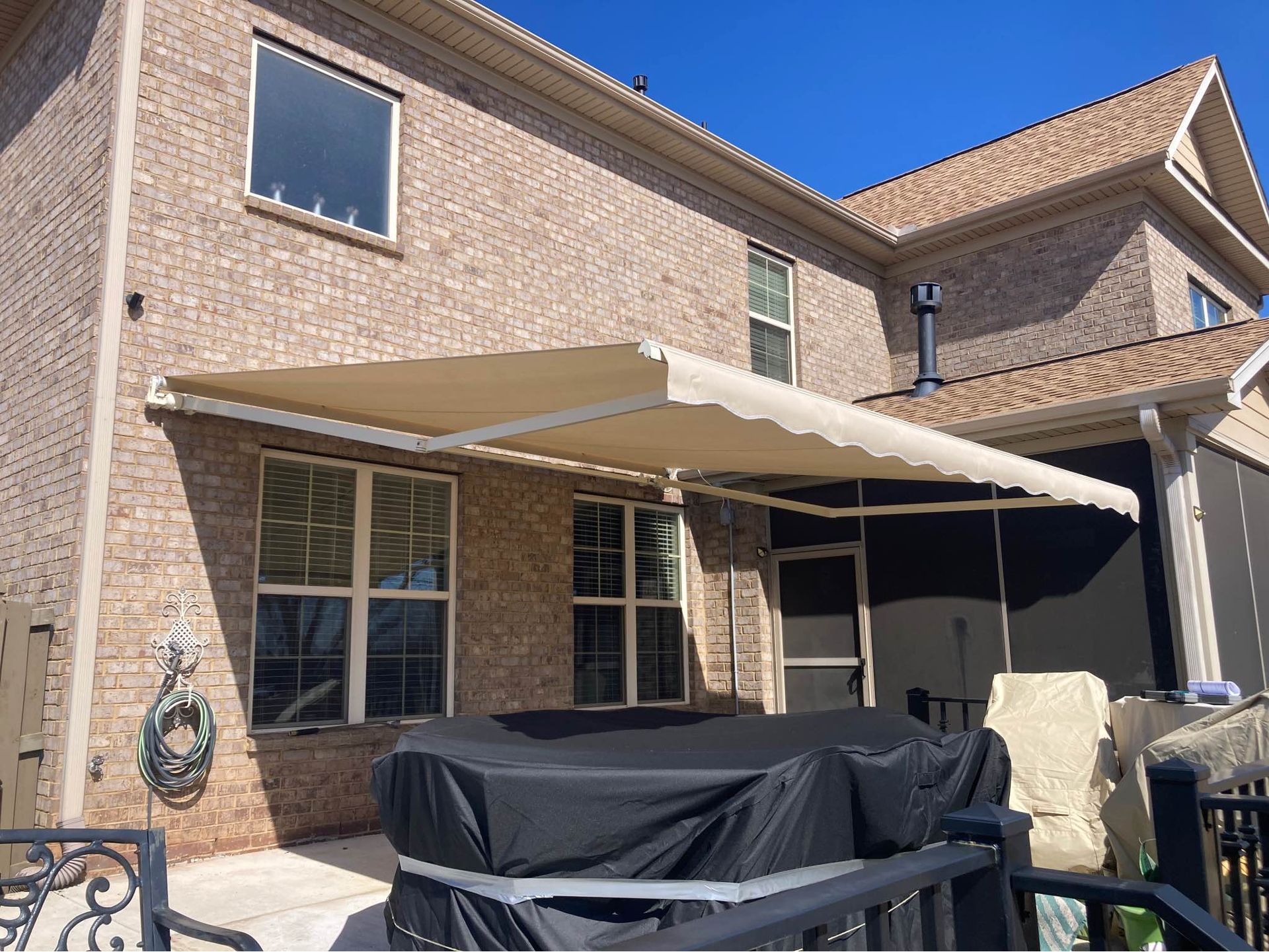 Beige retractable awning over a patio, attached to a brick house.