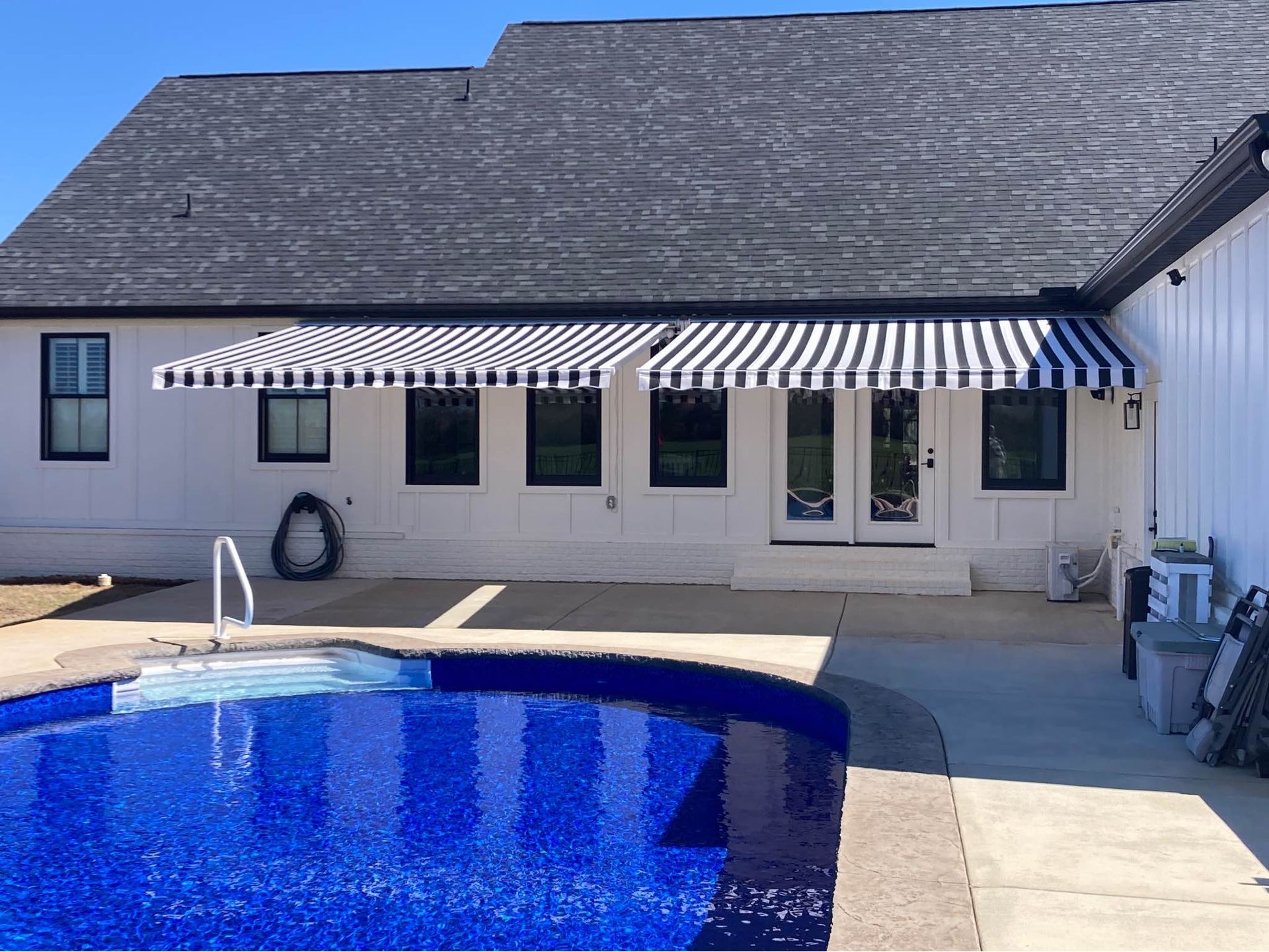 Pool with blue tile and white house with striped awning.