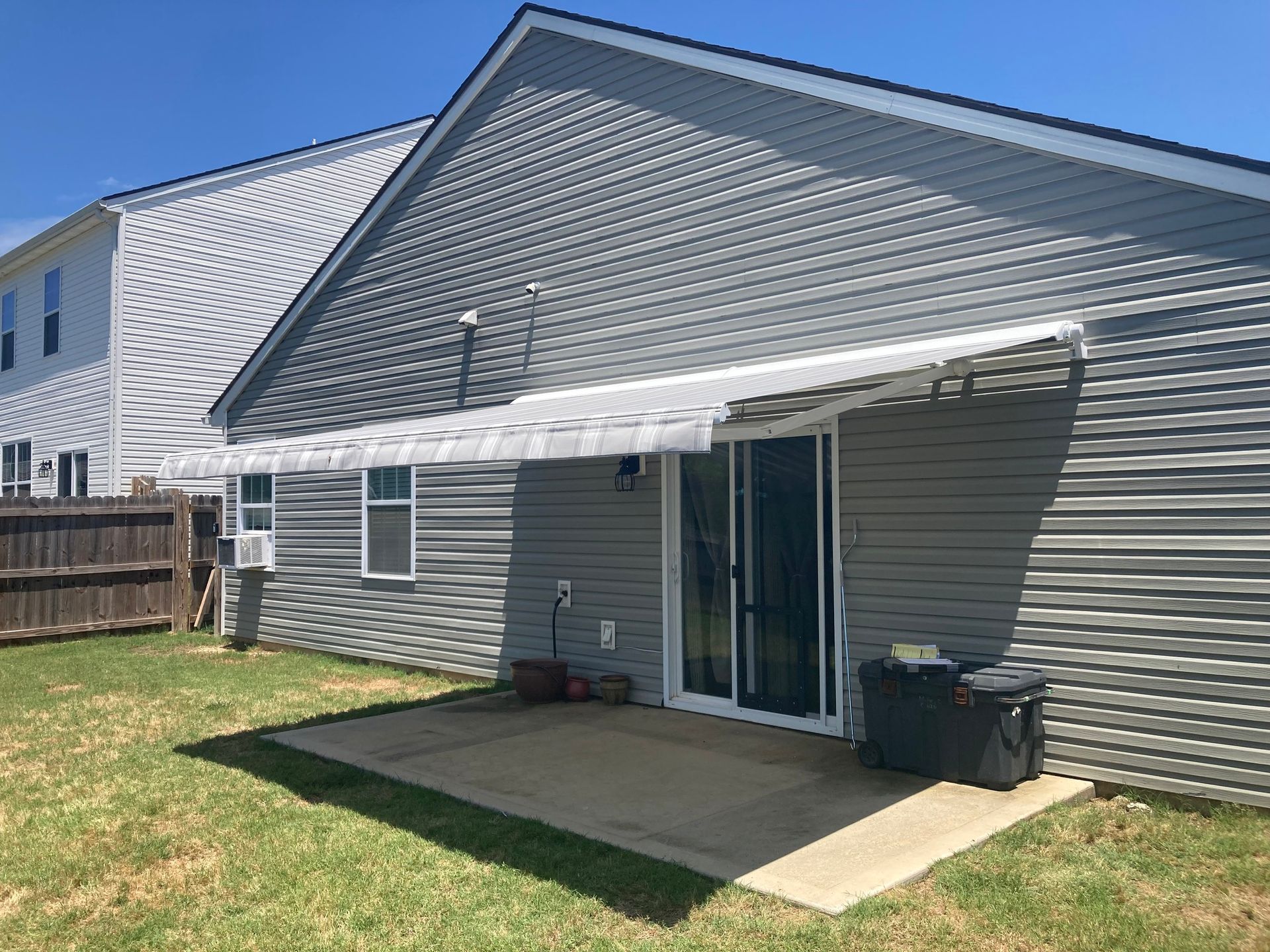 Backyard with grey siding, patio, sliding glass door, and a white awning.