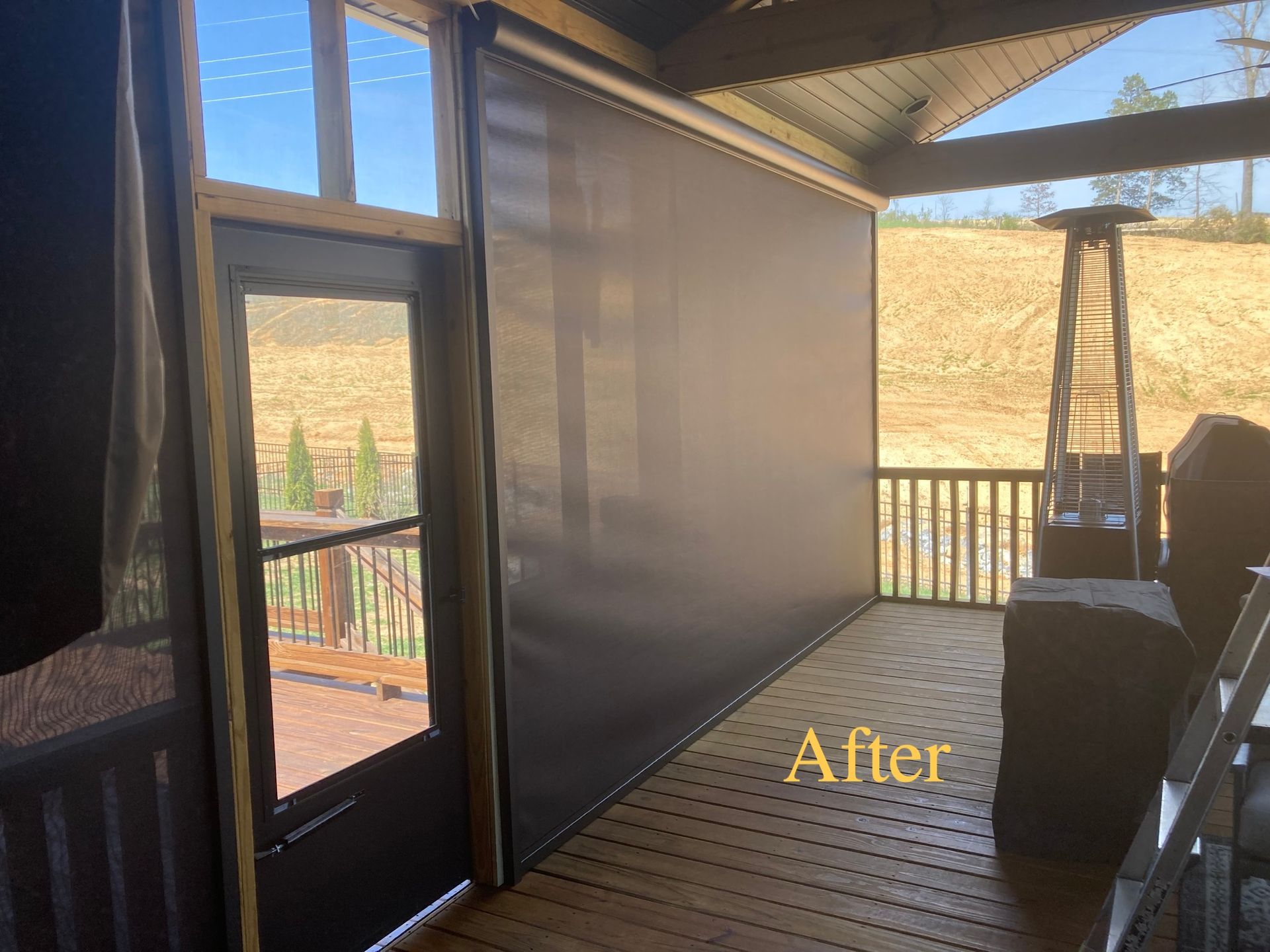 Outdoor deck with retractable screen, brown wood, and a view of a hillside.