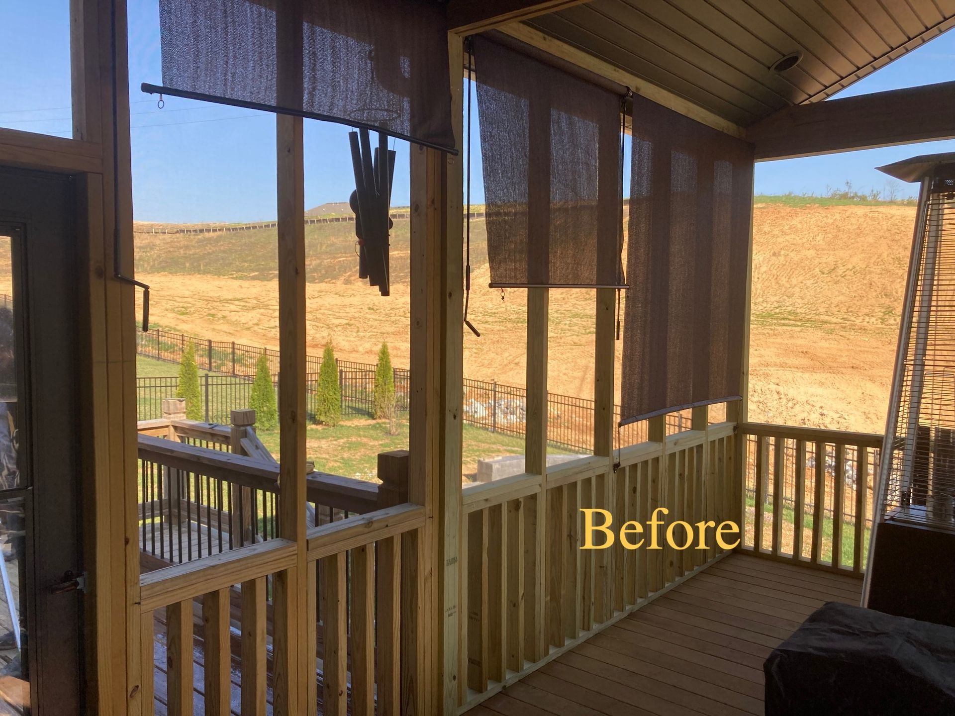 Exterior porch before remodeling. Wooden railing, shades, and sunny view of landscape.