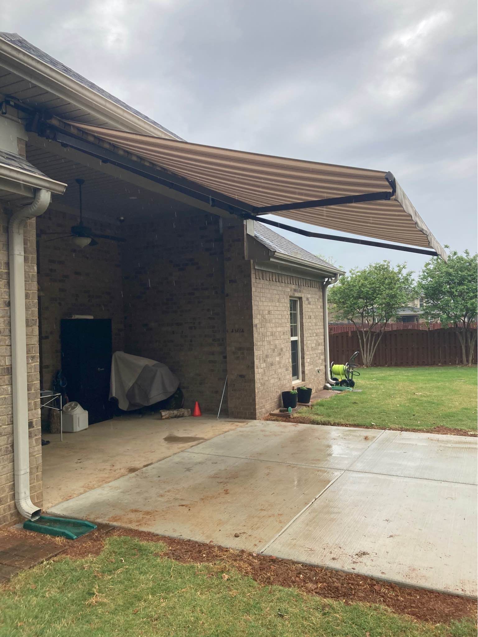 A brown and tan retractable awning extends from a brick building over a concrete patio.
