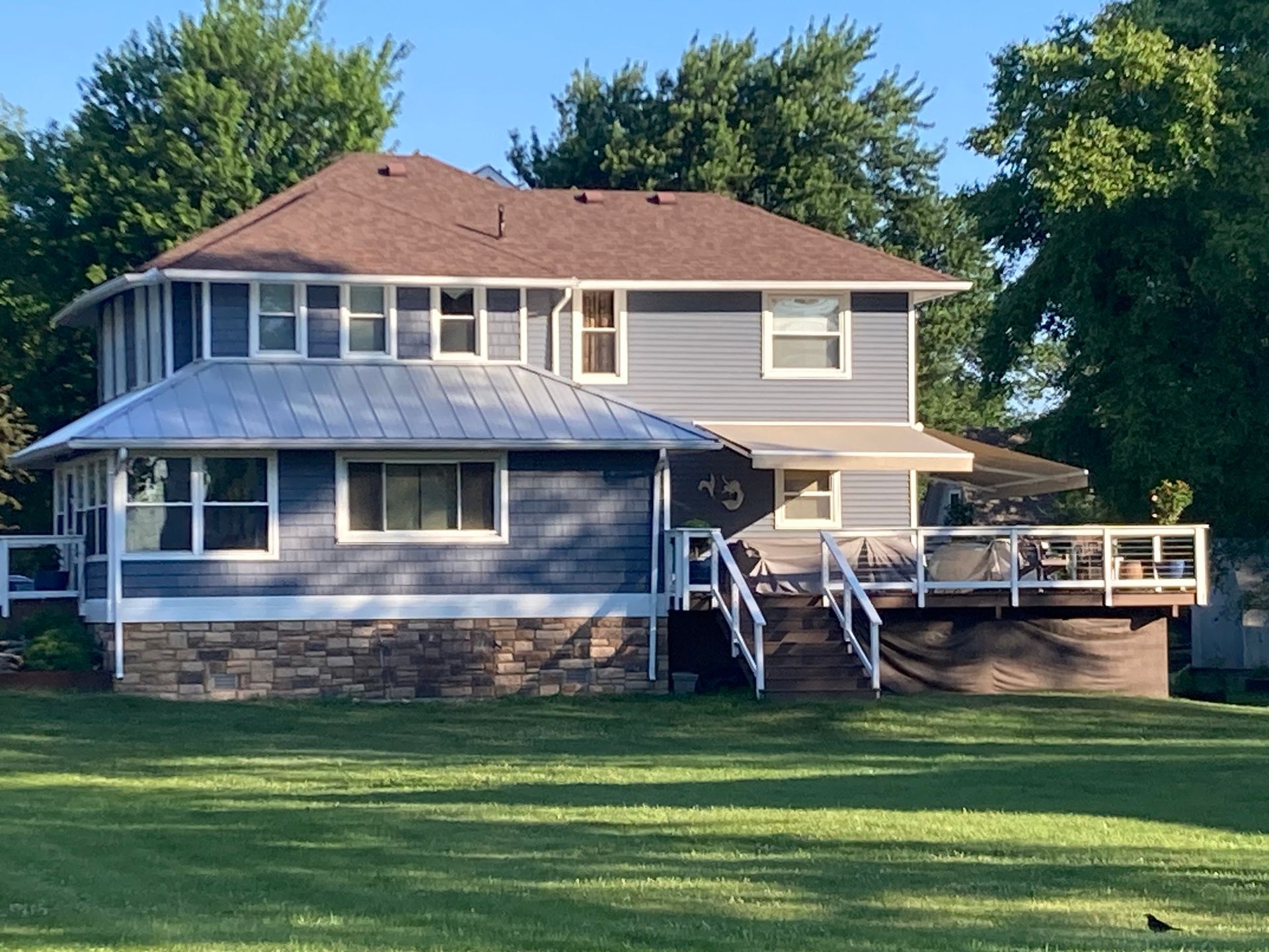 Blue house with brown roof, white trim, and a wrap-around deck on a green lawn.