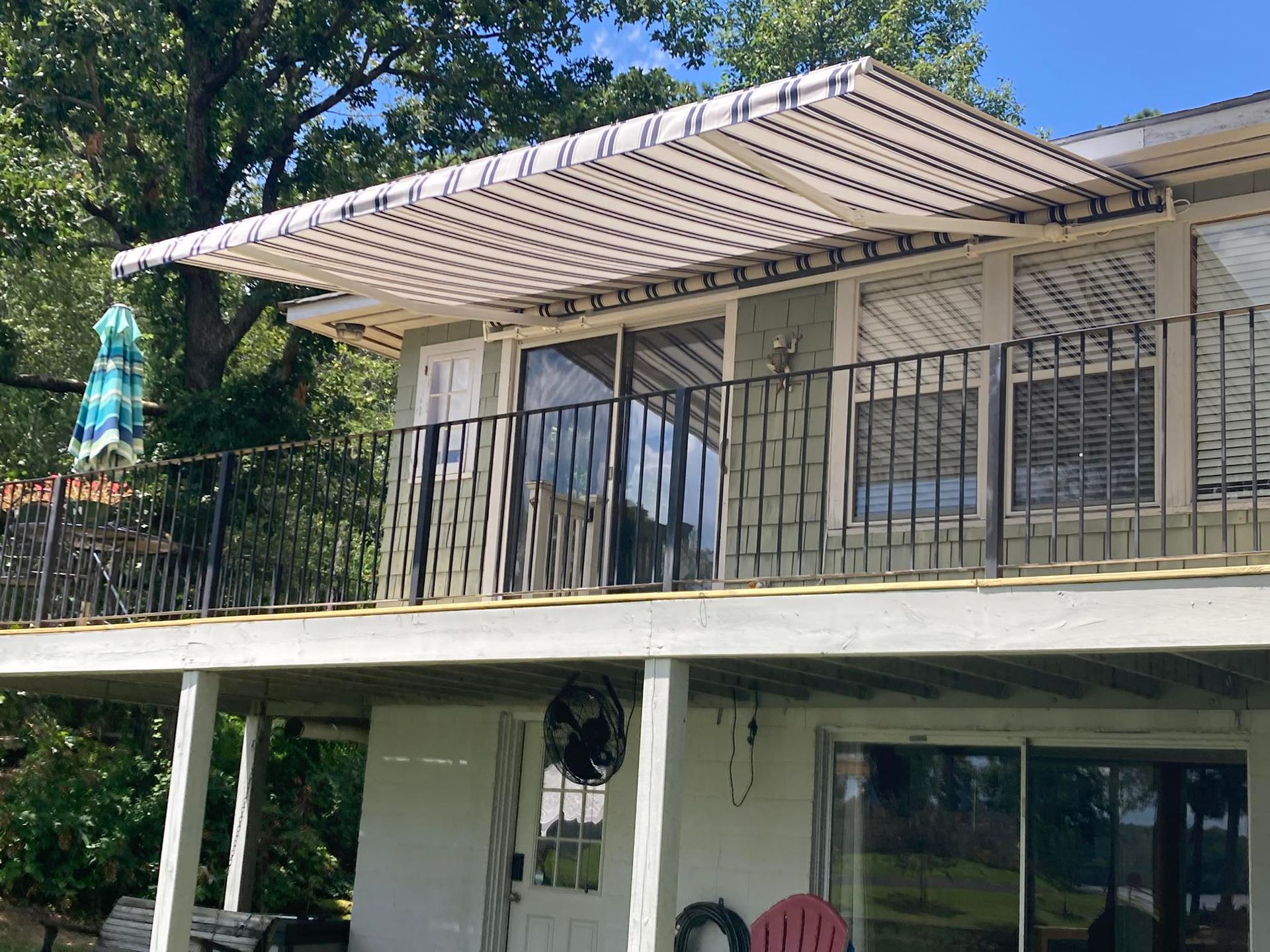 Balcony with awning, railing, and sliding doors on a two-story house. White and blue striped awning.