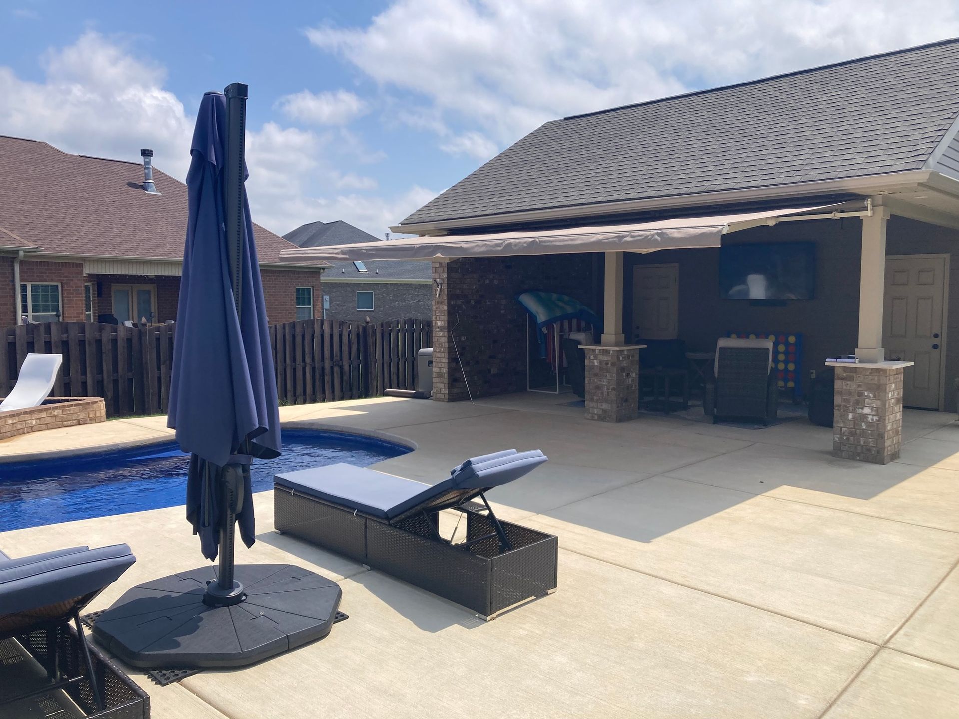 Poolside patio with an umbrella, lounge chairs, and a covered outdoor kitchen.