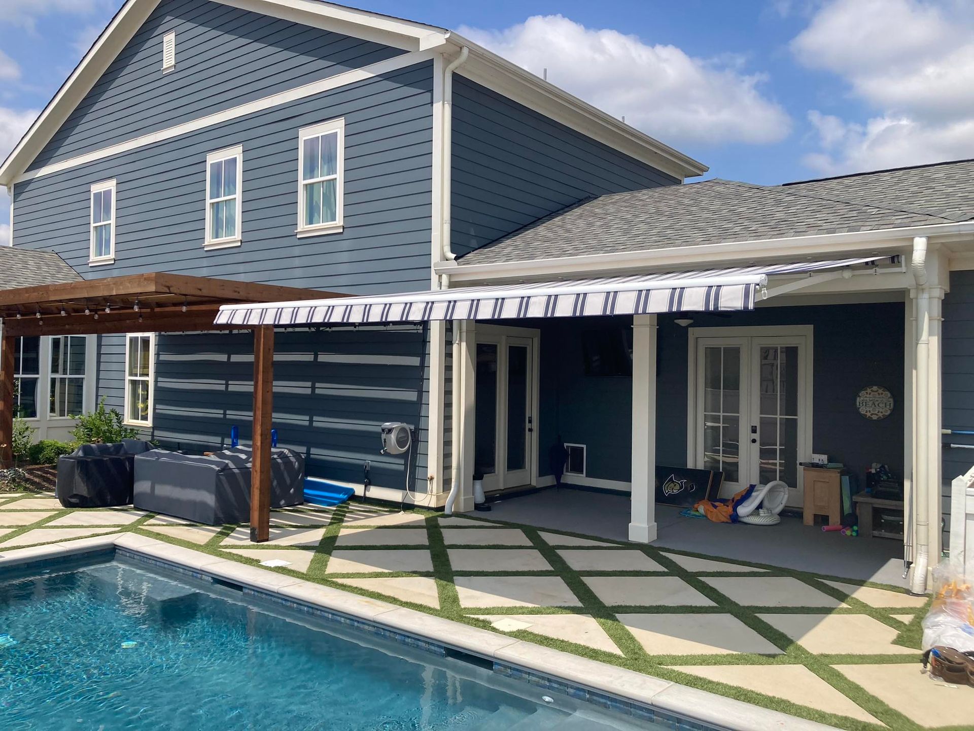 Blue house with a pool and patio. Awnings provide shade.