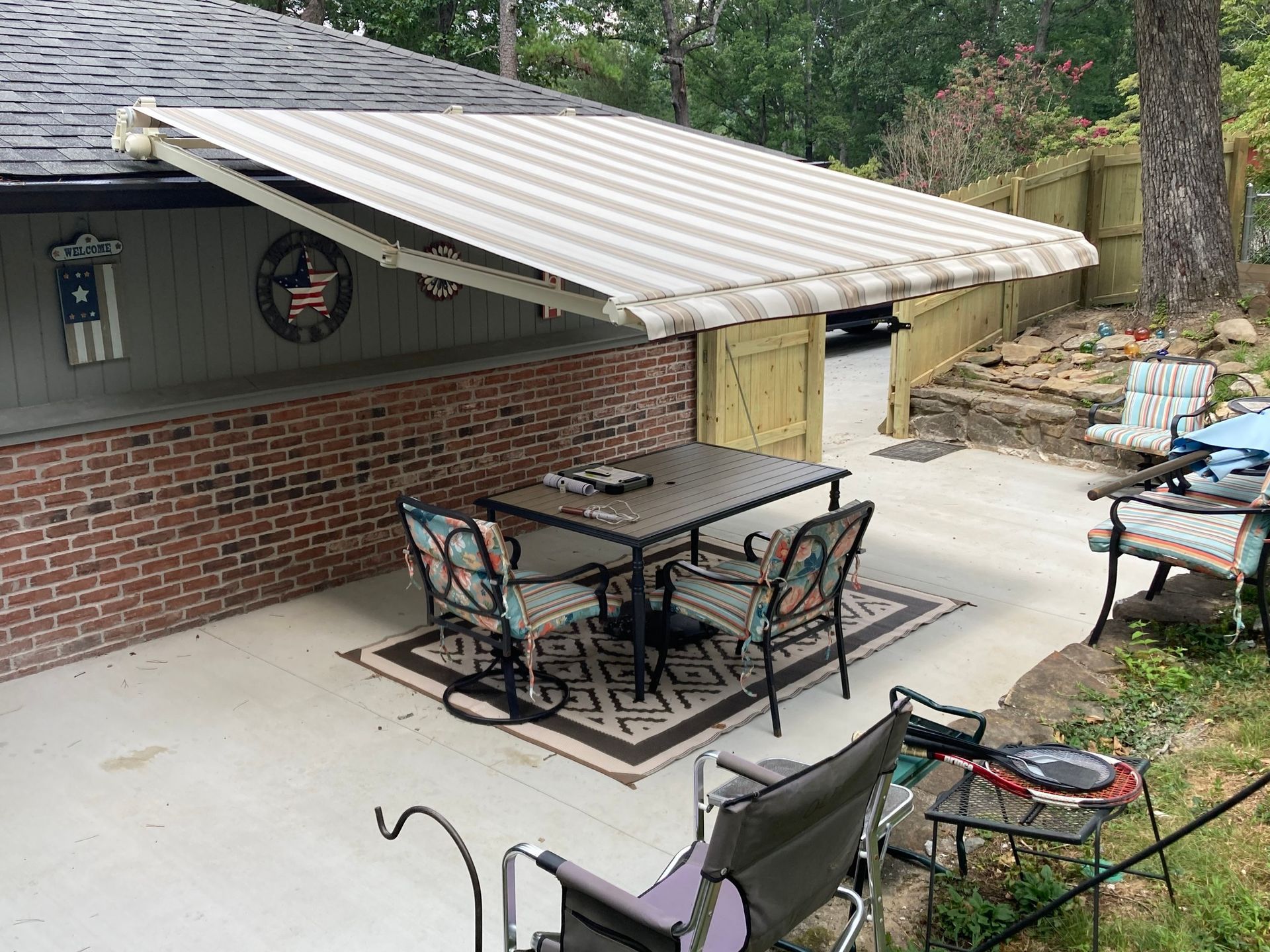 Patio with retractable striped awning over table and chairs, brick wall, concrete floor.