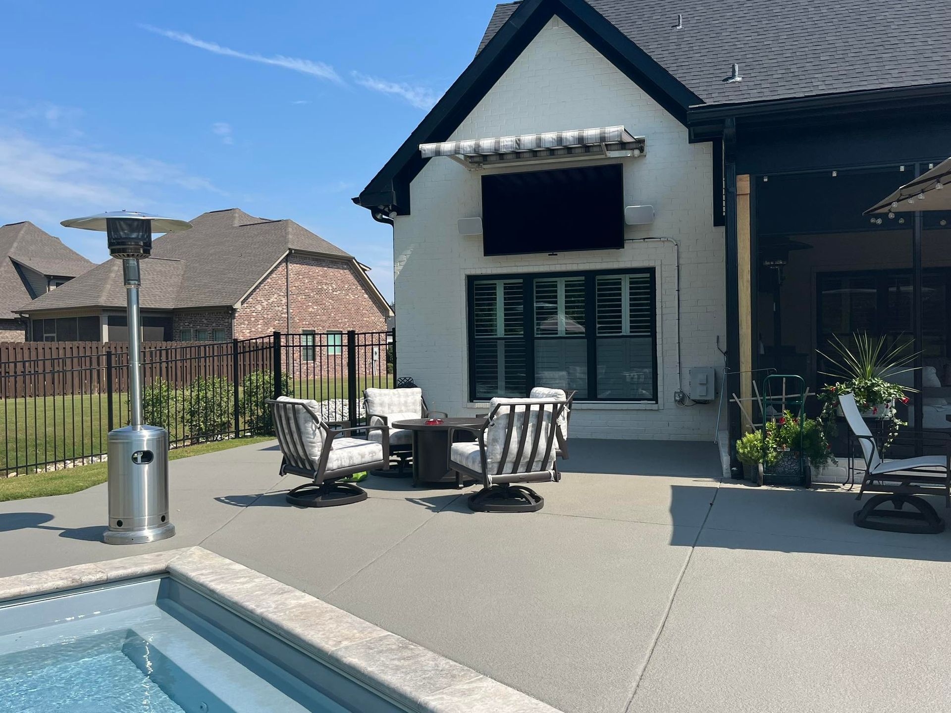 Patio with seating, outdoor TV, and a pool on a sunny day. A heater stands nearby.