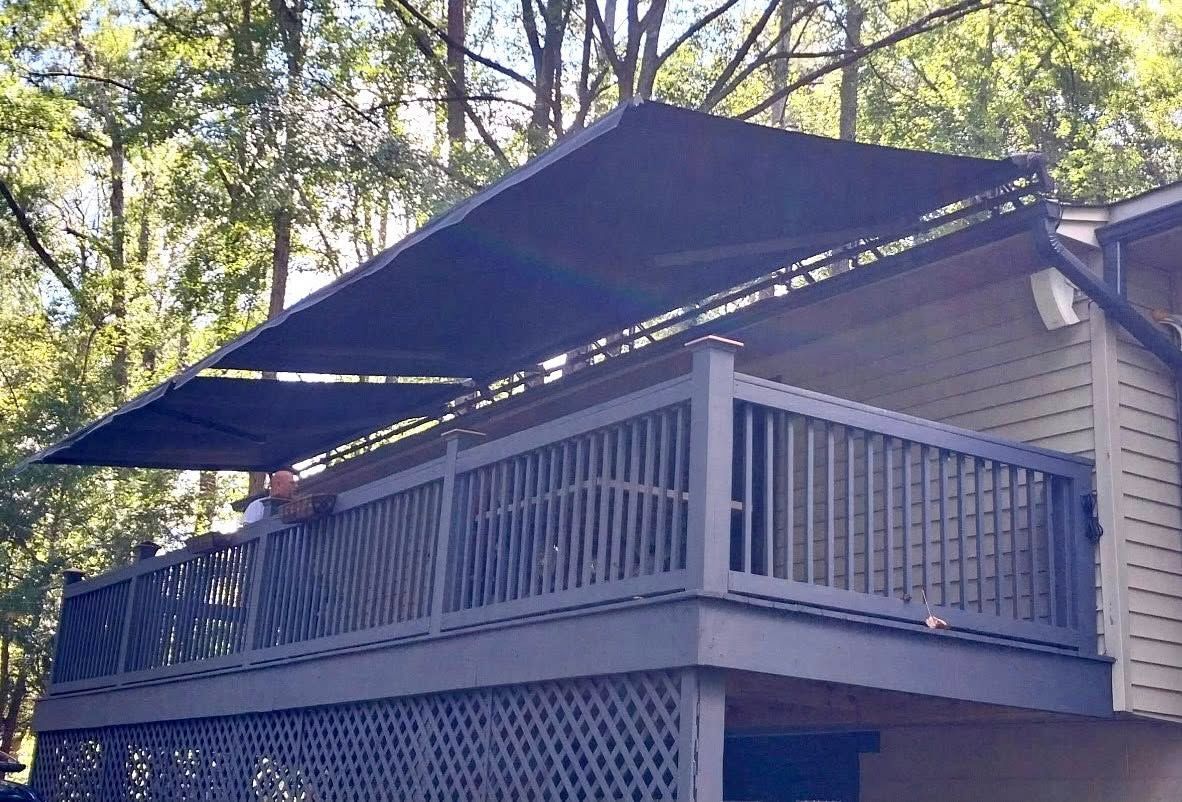 Black awning shades a gray deck with a dark railing. Trees in background.