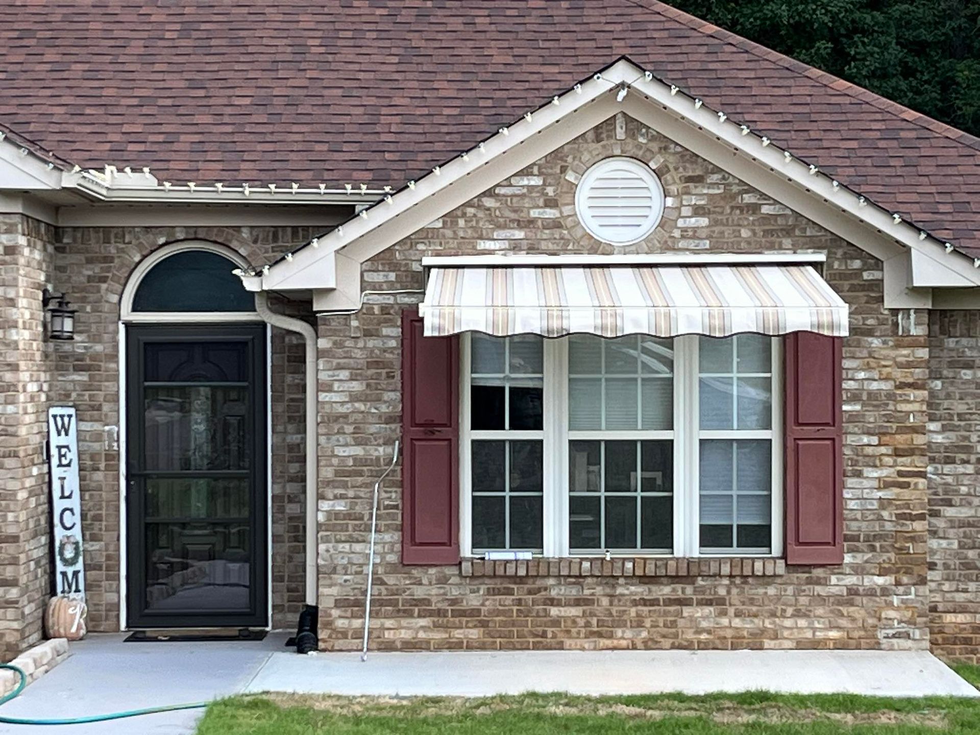 Brick house with awning over a window, red shutters, and 
