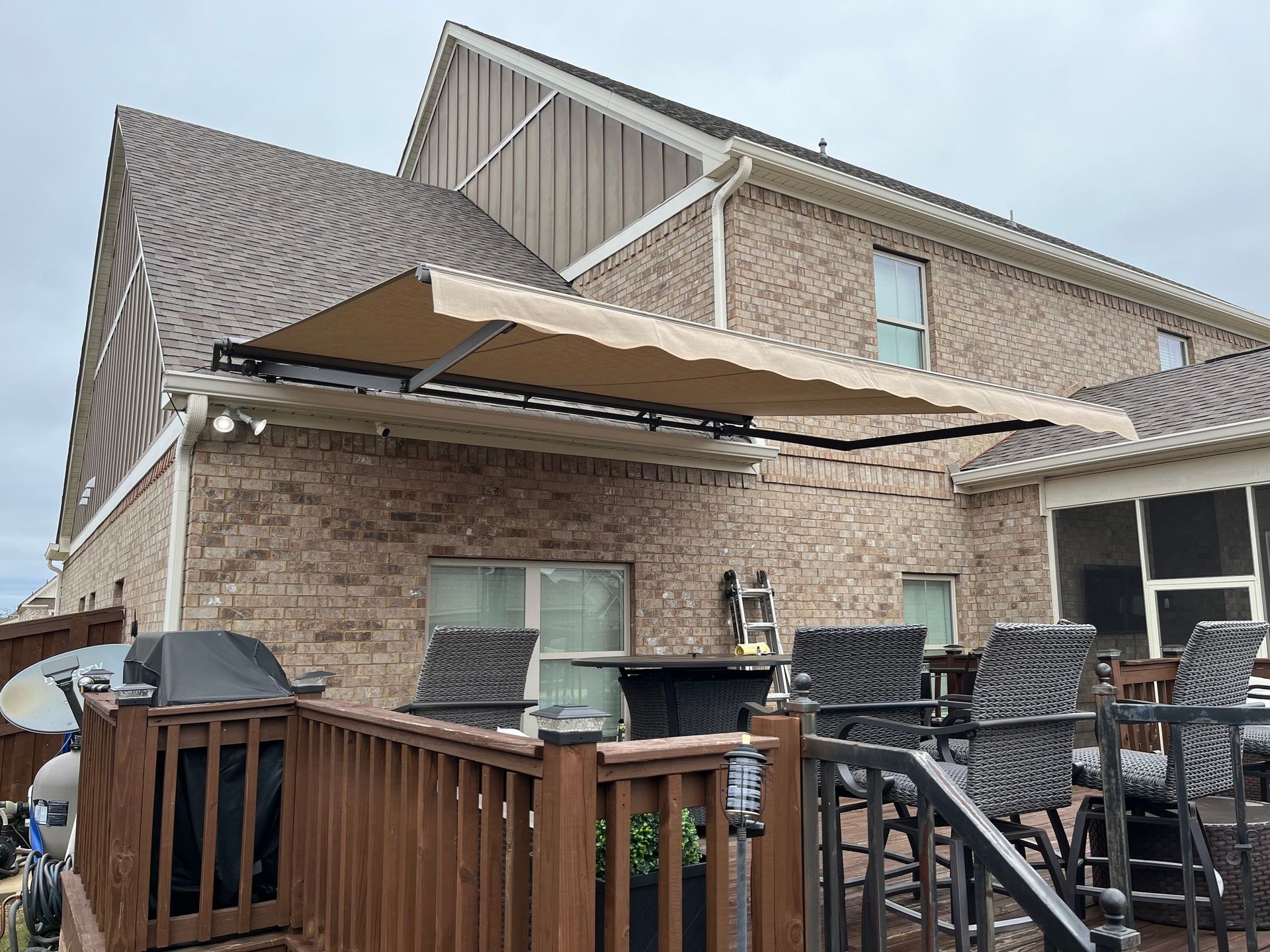 Beige retractable awning extends over a wooden deck attached to a brick house.