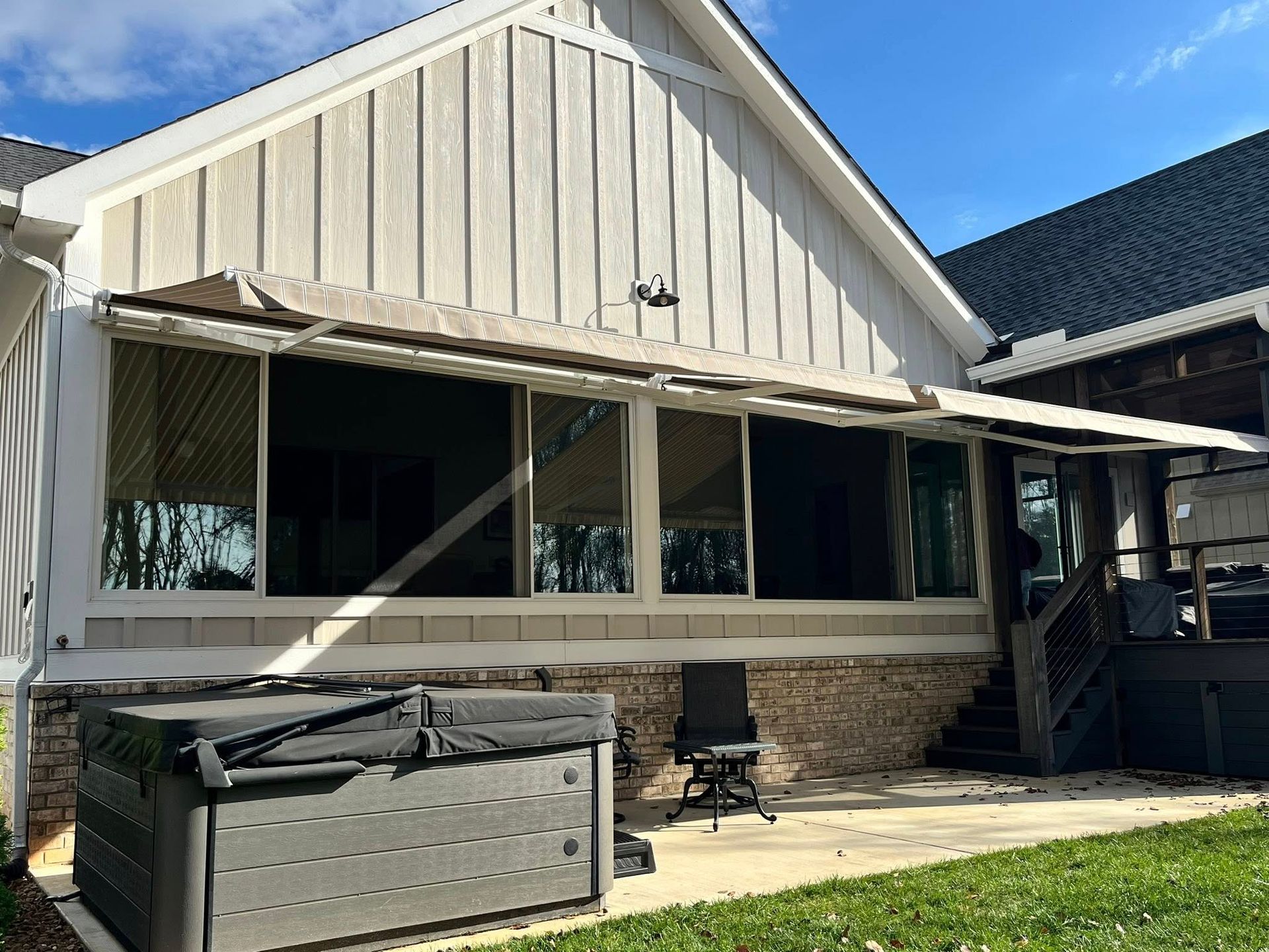 Beige awning over windows of a house with a hot tub and deck in the backyard.