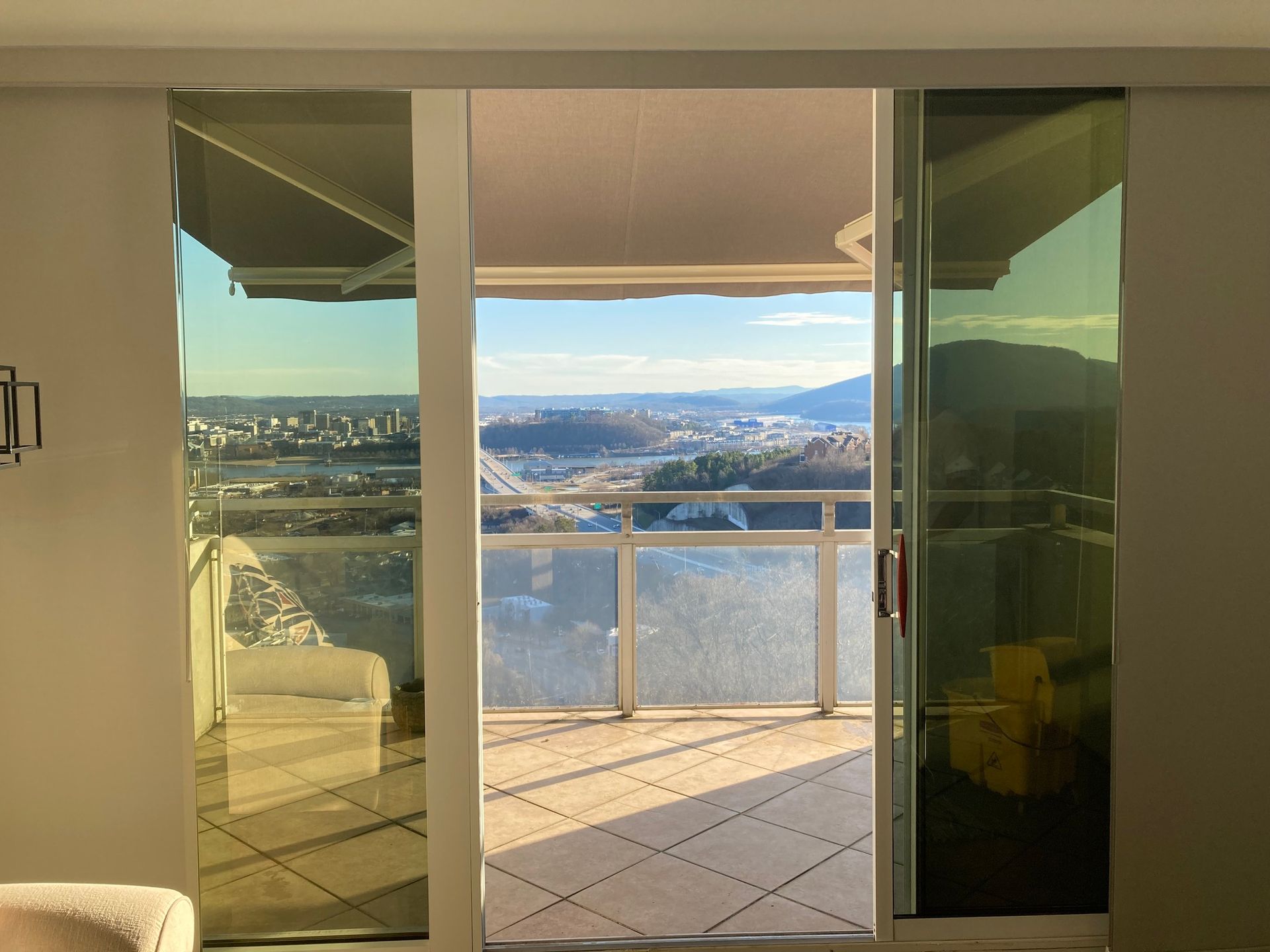 Sliding glass doors open onto a balcony with a city and mountains view on a sunny day.