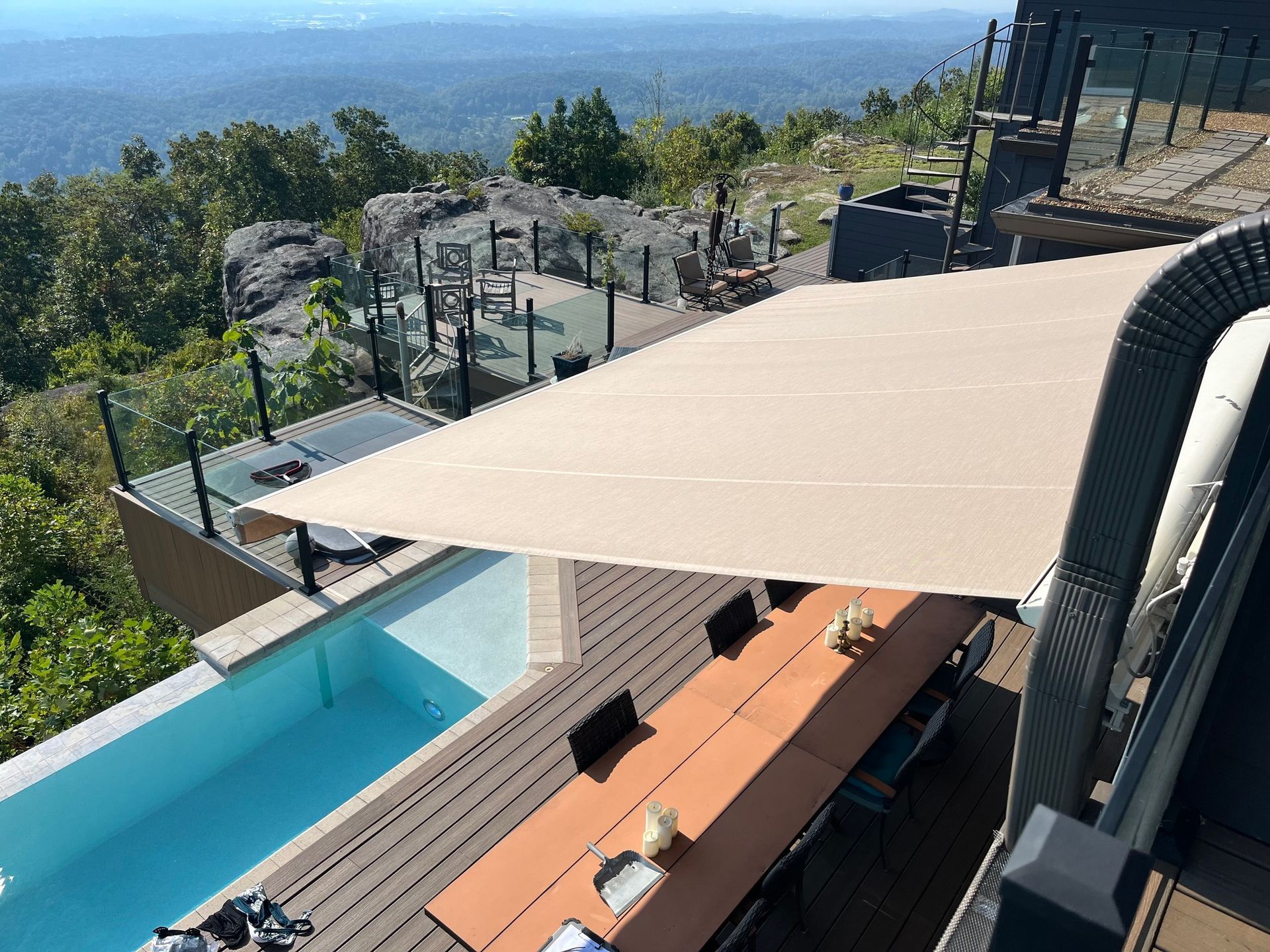 Poolside patio with long table shaded by a beige sail, overlooking mountain views.